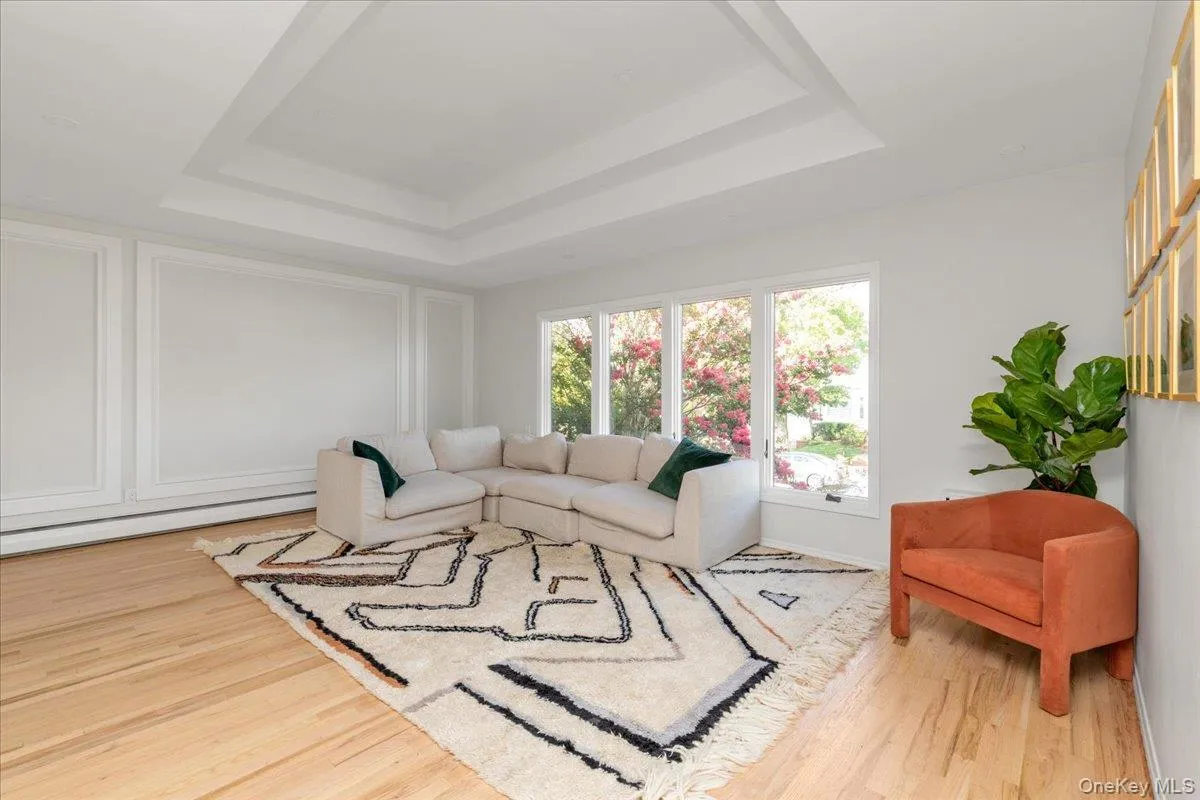 Living area featuring a raised ceiling, light wood-type flooring, a baseboard heating unit, and a decorative wall Living area featuring a raised ceiling, light wood-type flooring, a baseboard heating unit, and a decorative wall