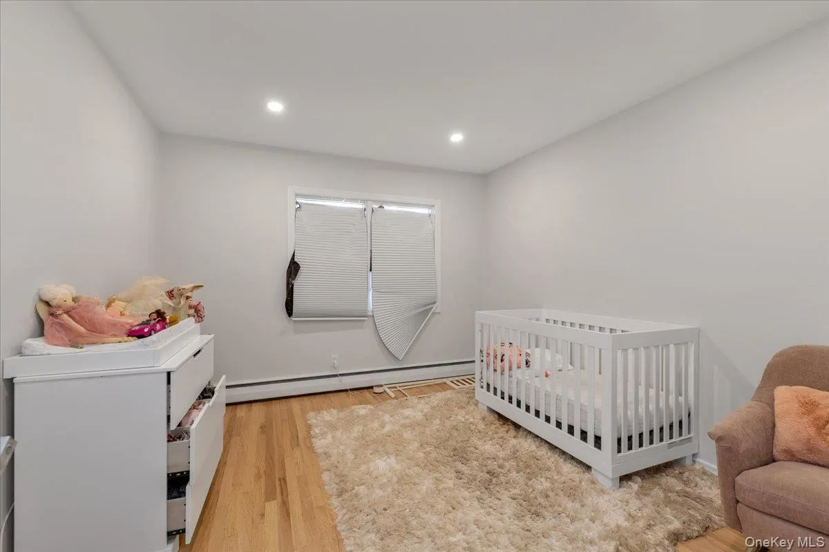 Bedroom featuring a crib, light wood finished floors, baseboard heating, and recessed lighting Bedroom featuring a crib, light wood finished floors, baseboard heating, and recessed lighting