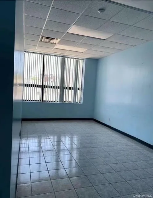 Empty room featuring tile patterned floors, a drop ceiling, and a smoke detector Empty room featuring tile patterned floors, a drop ceiling, and a smoke detector