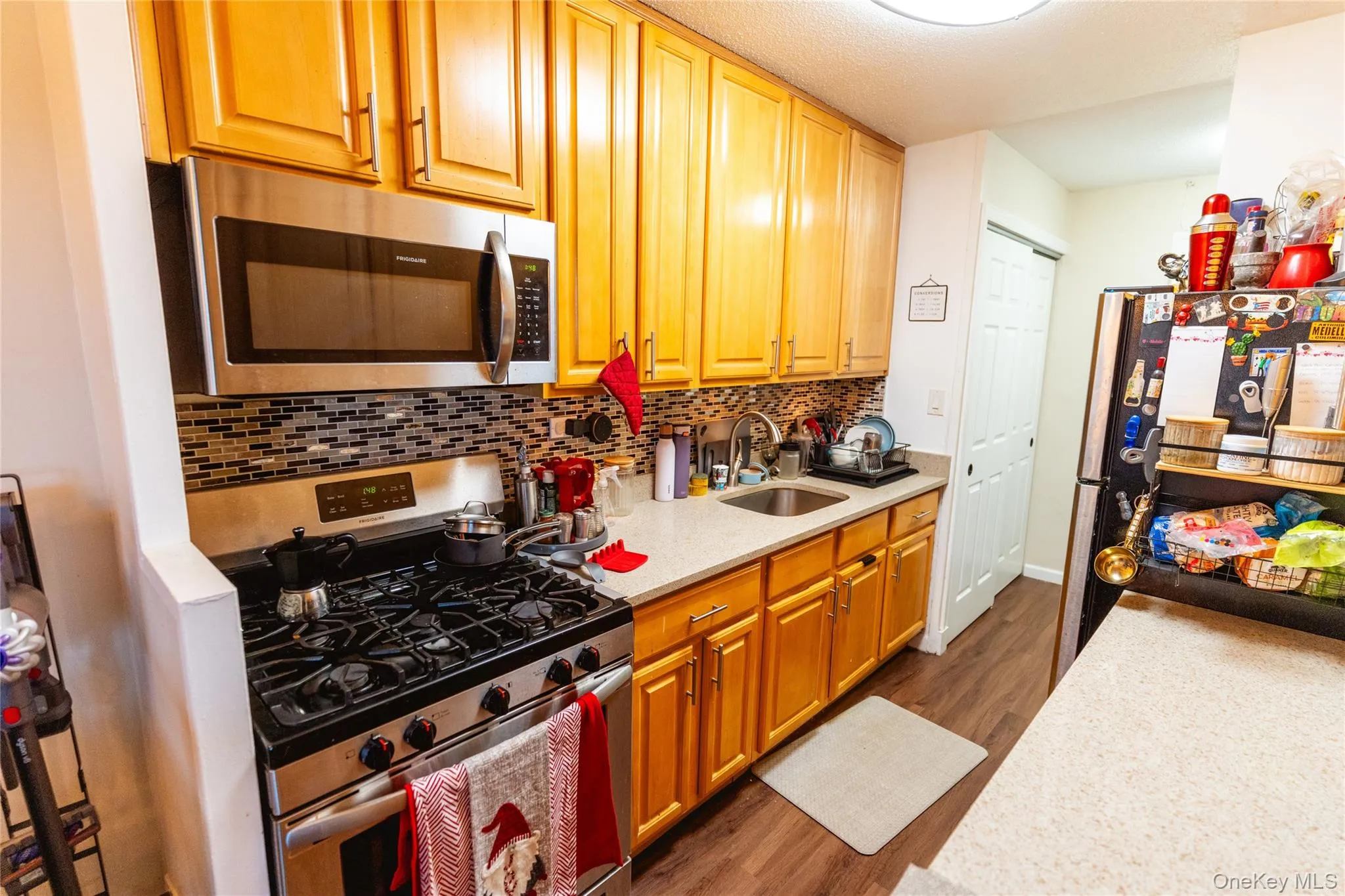 Kitchen with stainless steel appliances, dark wood-style flooring, light stone countertops, and backsplash Kitchen with stainless steel appliances, dark wood-style flooring, light stone countertops, and backsplash