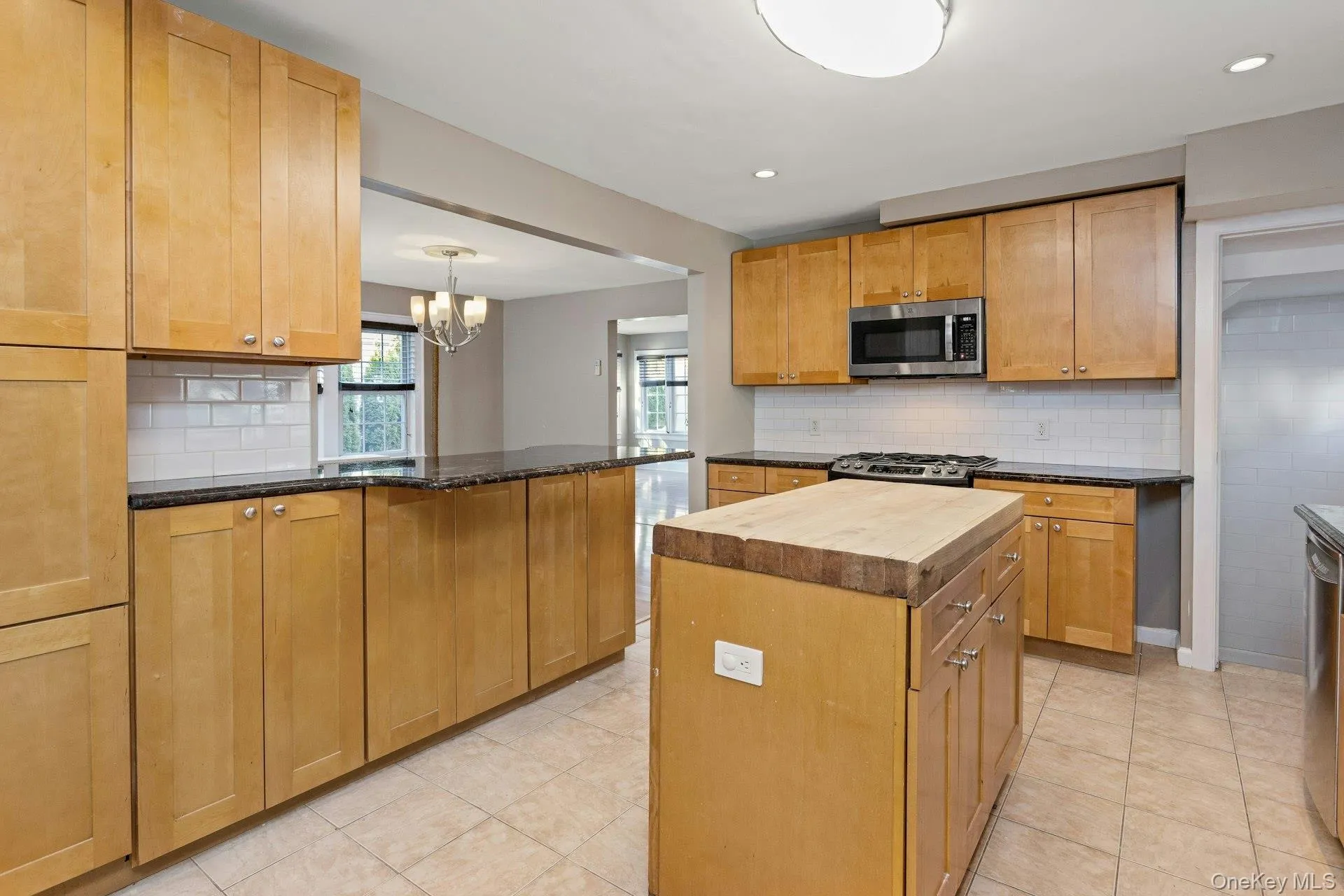 Kitchen with tasteful backsplash, wooden counters, stainless steel appliances, a peninsula, and a chandelier Kitchen with tasteful backsplash, wooden counters, stainless steel appliances, a peninsula, and a chandelier