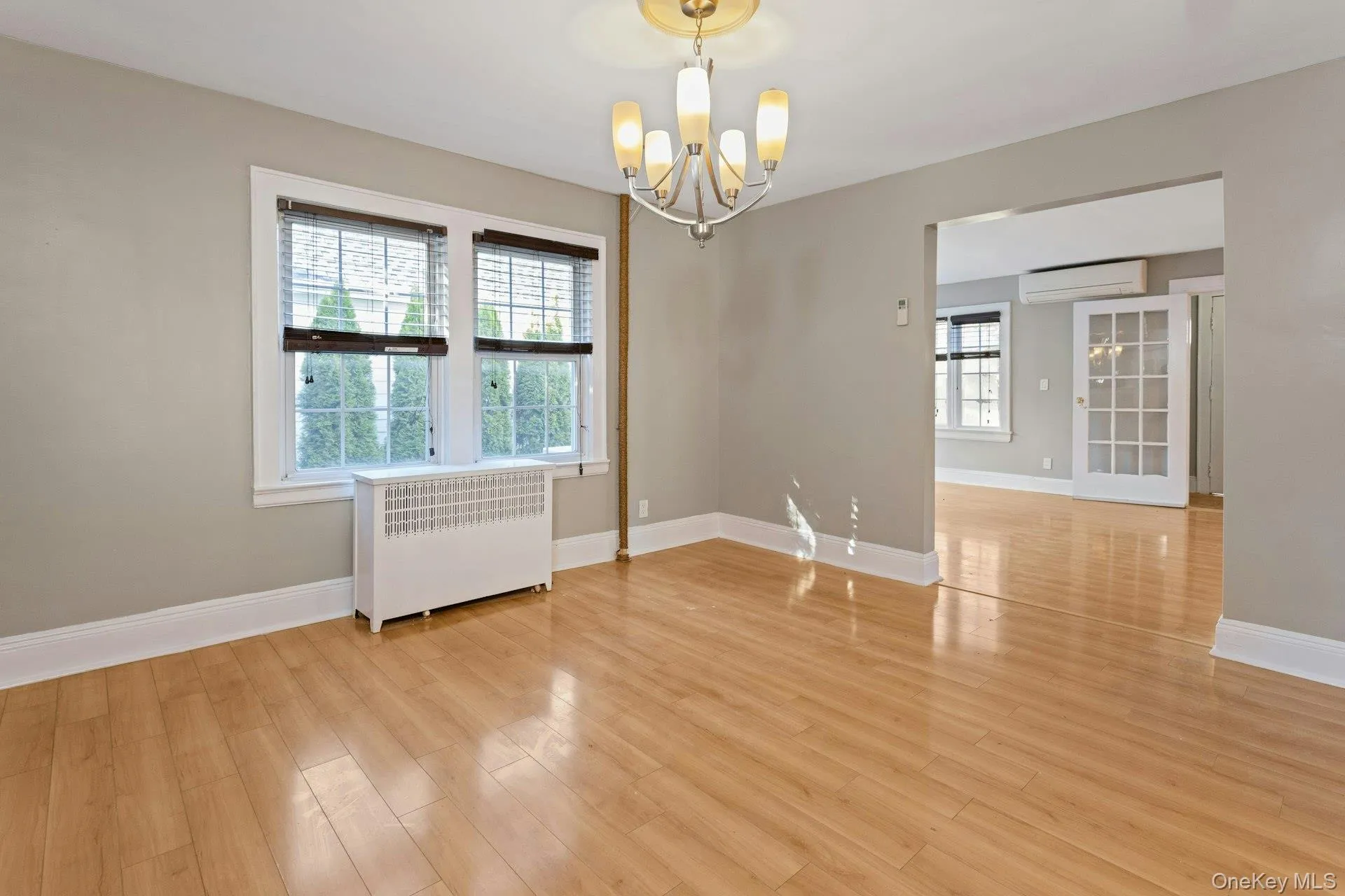 Spare room featuring radiator, a chandelier, light wood-type flooring, and an AC wall unit Spare room featuring radiator, a chandelier, light wood-type flooring, and an AC wall unit