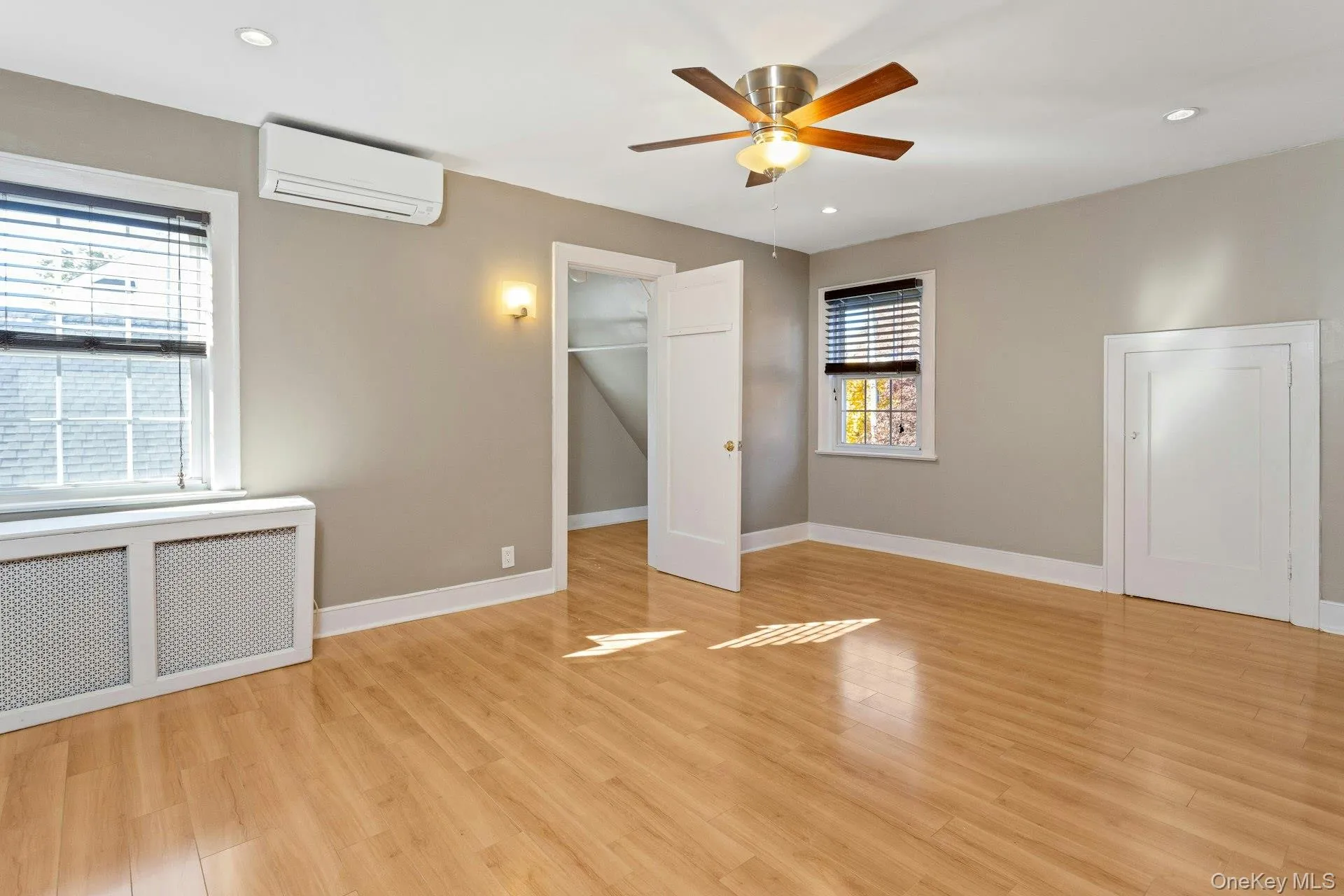 Unfurnished bedroom featuring radiator, a walk in closet, a wall mounted AC, light wood-style flooring, and recessed lighting Unfurnished bedroom featuring radiator, a walk in closet, a wall mounted AC, light wood-style flooring, and recessed lighting