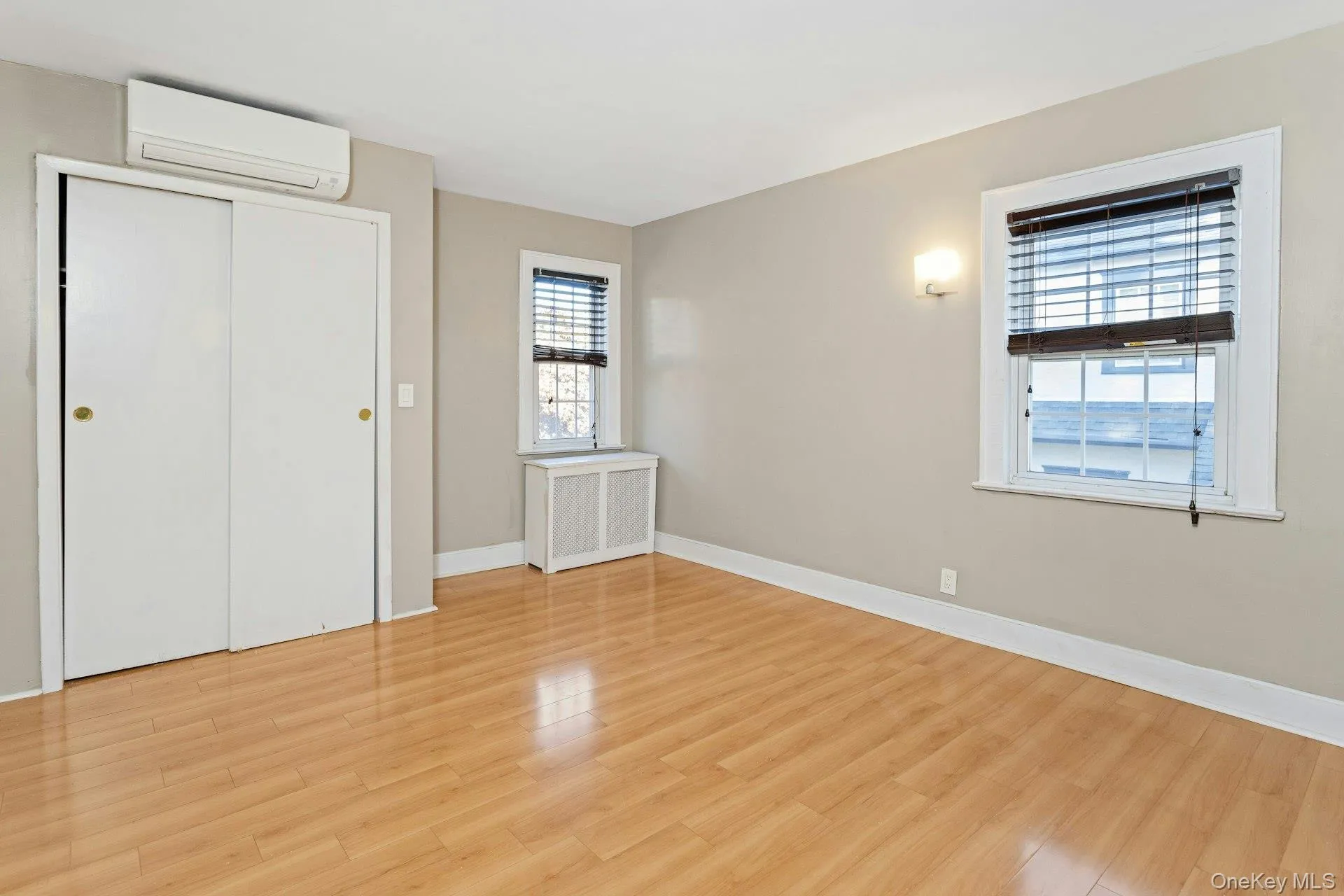 Unfurnished bedroom with a wall mounted air conditioner, radiator, light wood-type flooring, and a closet Unfurnished bedroom with a wall mounted air conditioner, radiator, light wood-type flooring, and a closet