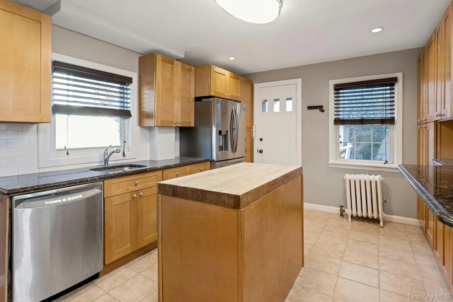 Kitchen featuring butcher block countertops, decorative backsplash, stainless steel appliances, radiator, and light tile patterned floors Kitchen featuring butcher block countertops, decorative backsplash, stainless steel appliances, radiator, and light tile patterned floors