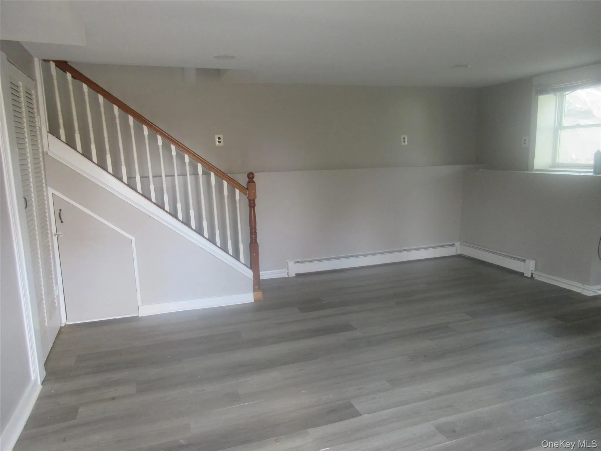Unfurnished living room with wood finished floors, a baseboard radiator, and stairs Unfurnished living room with wood finished floors, a baseboard radiator, and stairs