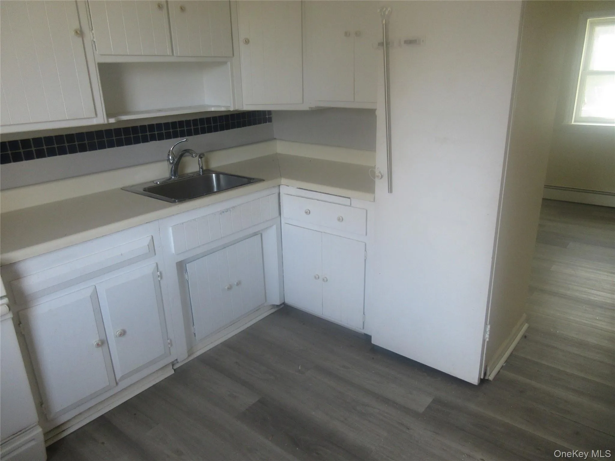 Kitchen featuring dark wood-style flooring, light countertops, and white cabinets Kitchen featuring dark wood-style flooring, light countertops, and white cabinets