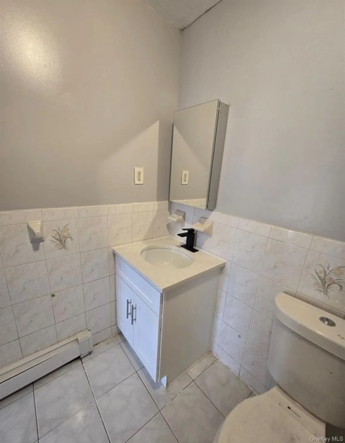 Bathroom featuring tile walls, a baseboard radiator, light tile patterned flooring, wainscoting, and vanity Bathroom featuring tile walls, a baseboard radiator, light tile patterned flooring, wainscoting, and vanity
