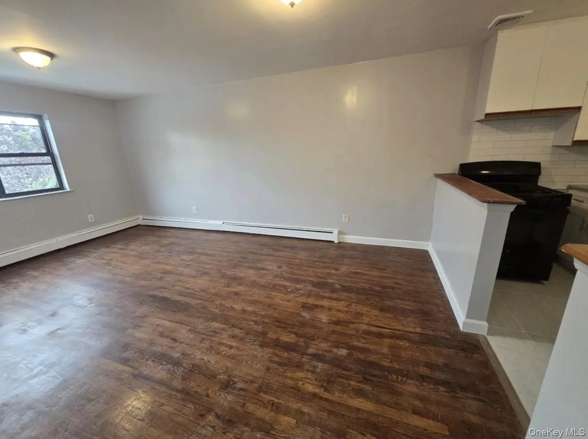 Unfurnished living room with dark wood-style floors and baseboard heating Unfurnished living room with dark wood-style floors and baseboard heating