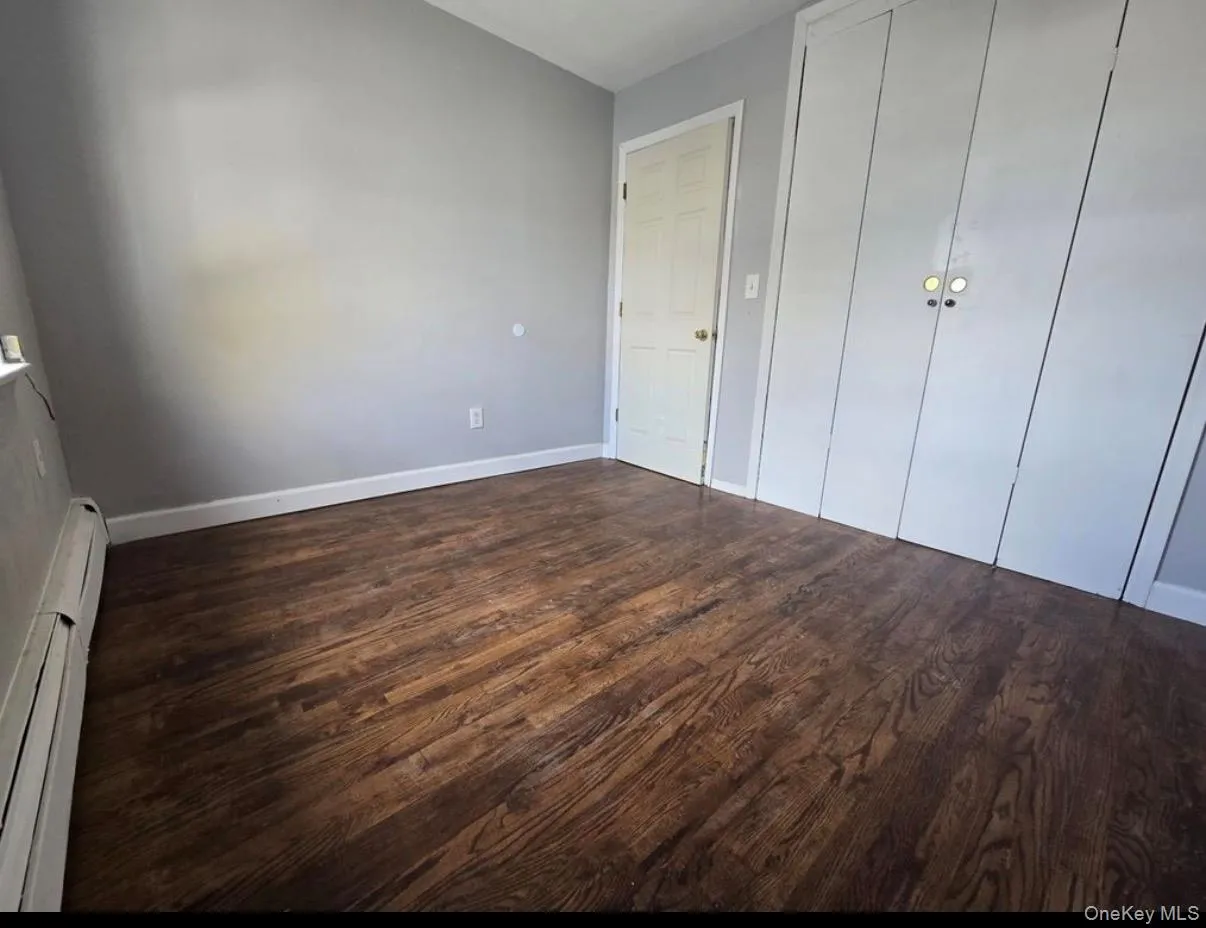 Unfurnished bedroom featuring a baseboard heating unit, dark wood-style flooring, and a closet Unfurnished bedroom featuring a baseboard heating unit, dark wood-style flooring, and a closet