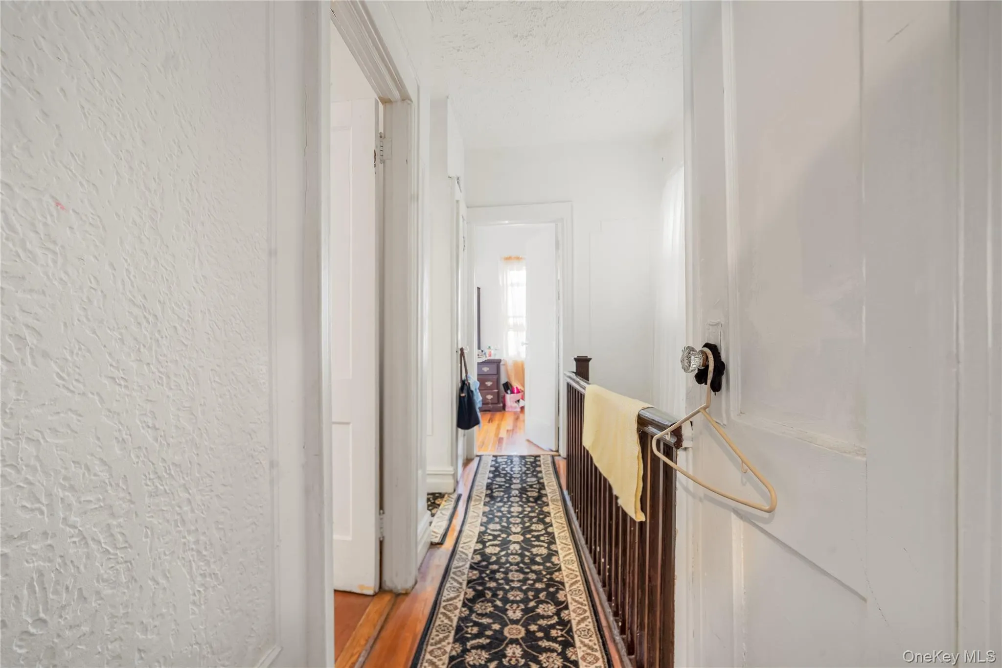 Hallway featuring dark wood-style floors, a textured ceiling, an upstairs landing, and a textured wall Hallway featuring dark wood-style floors, a textured ceiling, an upstairs landing, and a textured wall