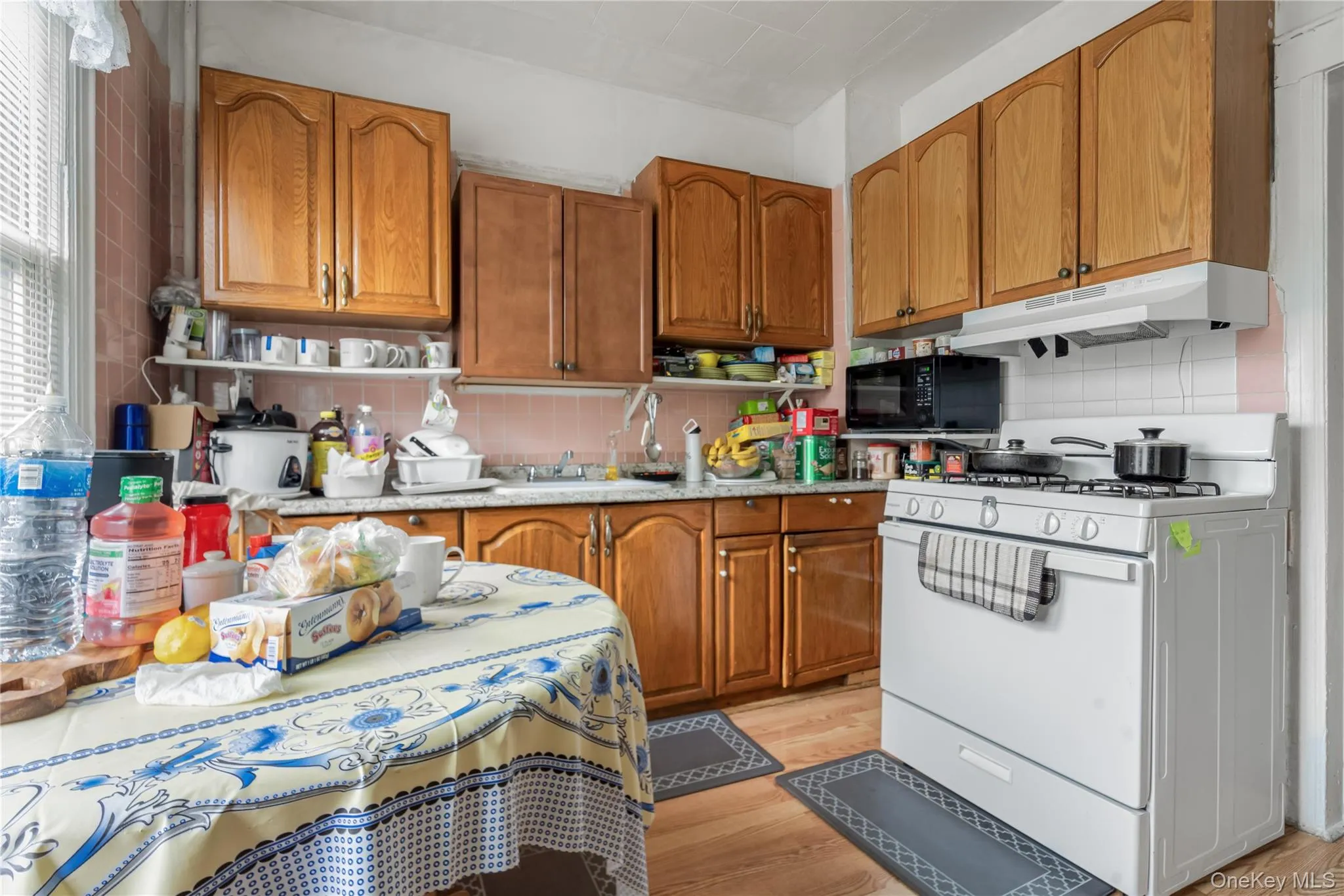 Kitchen featuring white range with gas stovetop, brown cabinets, light wood-style floors, black microwave, and backsplash Kitchen featuring white range with gas stovetop, brown cabinets, light wood-style floors, black microwave, and backsplash