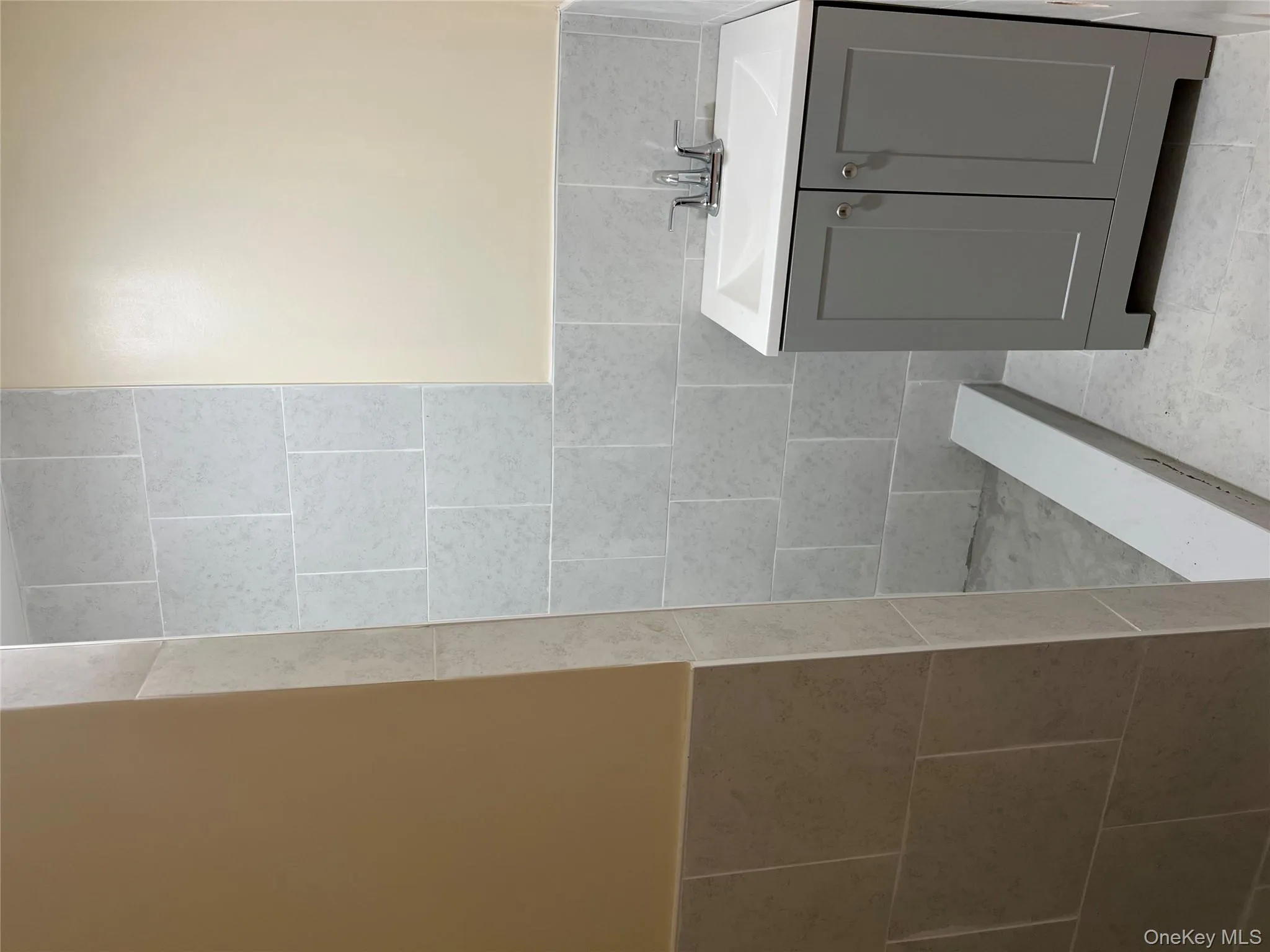 Full bath with tile walls, vanity, a wainscoted wall, light tile patterned floors, and a tile shower Full bath with tile walls, vanity, a wainscoted wall, light tile patterned floors, and a tile shower