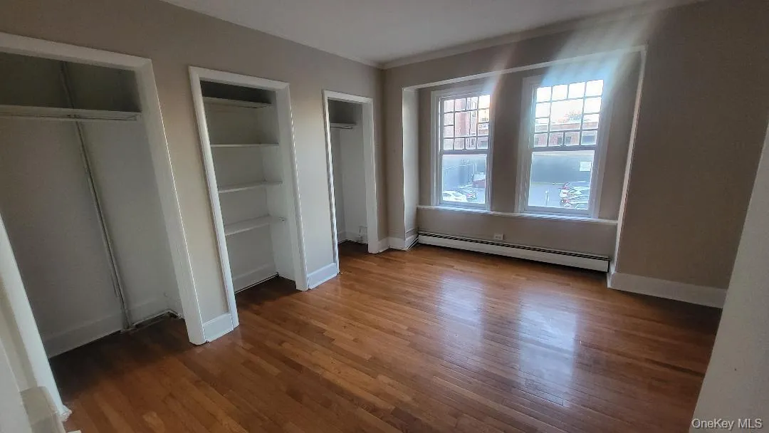 Unfurnished bedroom with multiple closets, wood finished floors, and a baseboard radiator Unfurnished bedroom with multiple closets, wood finished floors, and a baseboard radiator