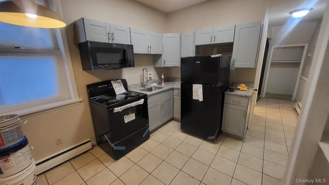 Kitchen featuring gray cabinets, black appliances, light tile patterned floors, baseboard heating, and light countertops Kitchen featuring gray cabinets, black appliances, light tile patterned floors, baseboard heating, and light countertops