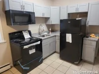 Kitchen with black appliances, light countertops, light tile patterned flooring, and a baseboard radiator Kitchen with black appliances, light countertops, light tile patterned flooring, and a baseboard radiator