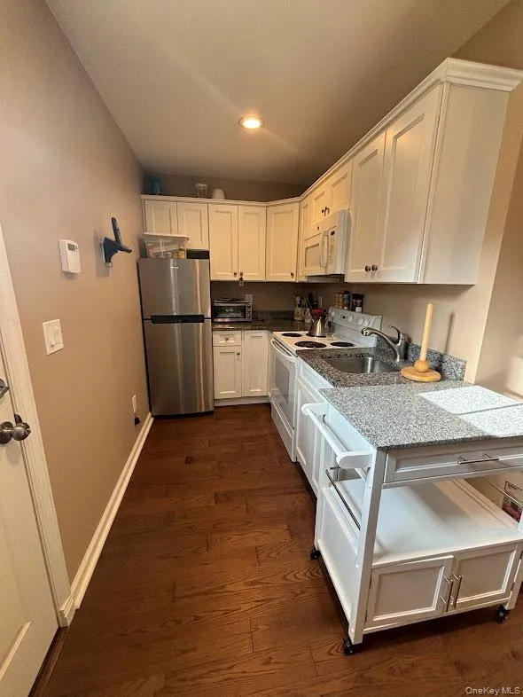 Kitchen featuring white cabinets, white appliances, dark wood finished floors, dark stone counters, and recessed lighting Kitchen featuring white cabinets, white appliances, dark wood finished floors, dark stone counters, and recessed lighting