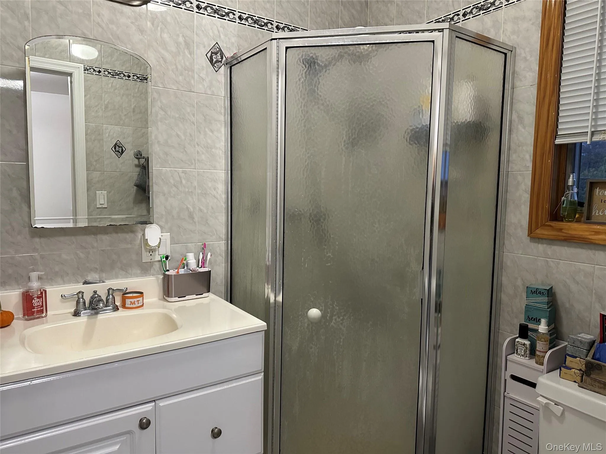 Bathroom featuring tile walls, backsplash, a shower stall, and vanity Bathroom featuring tile walls, backsplash, a shower stall, and vanity