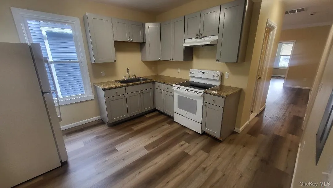 Kitchen featuring gray cabinets, white appliances, dark wood-type flooring, and under cabinet range hood Kitchen featuring gray cabinets, white appliances, dark wood-type flooring, and under cabinet range hood