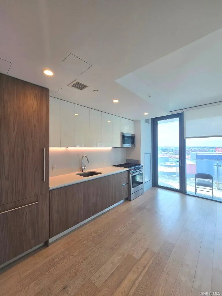 Kitchen featuring modern cabinets, white cabinetry, appliances with stainless steel finishes, light wood finished floors, and a wall of windows Kitchen featuring modern cabinets, white cabinetry, appliances with stainless steel finishes, light wood finished floors, and a wall of windows