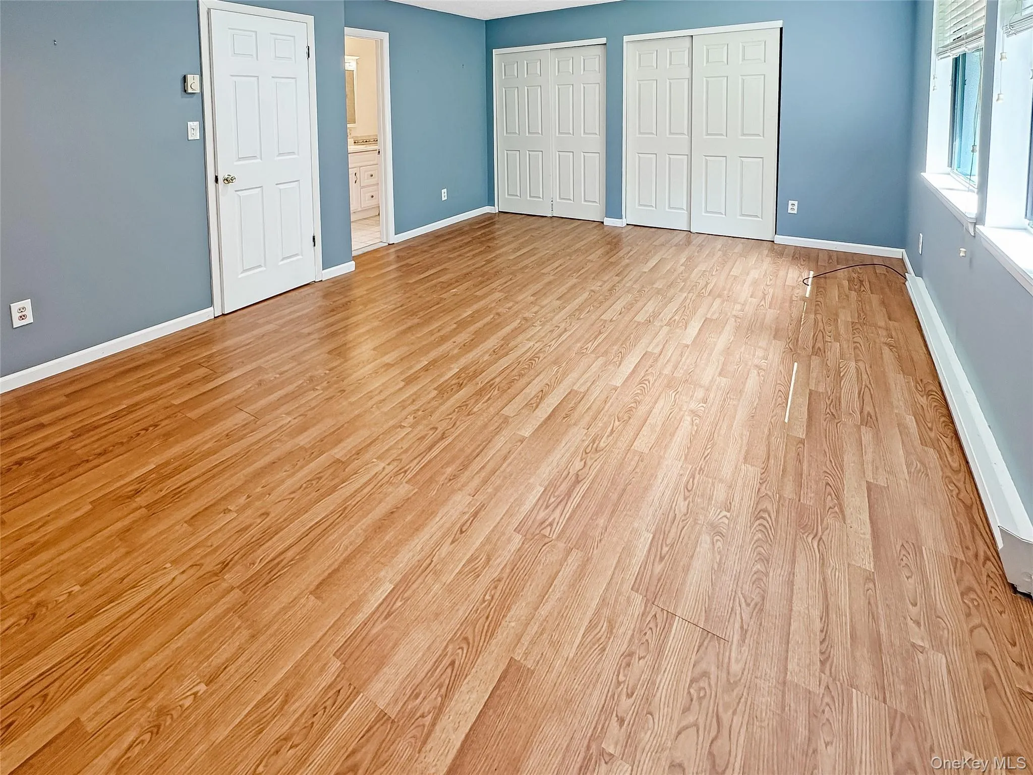 Unfurnished bedroom with multiple closets, a baseboard heating unit, light wood-type flooring, and connected bathroom Unfurnished bedroom with multiple closets, a baseboard heating unit, light wood-type flooring, and connected bathroom