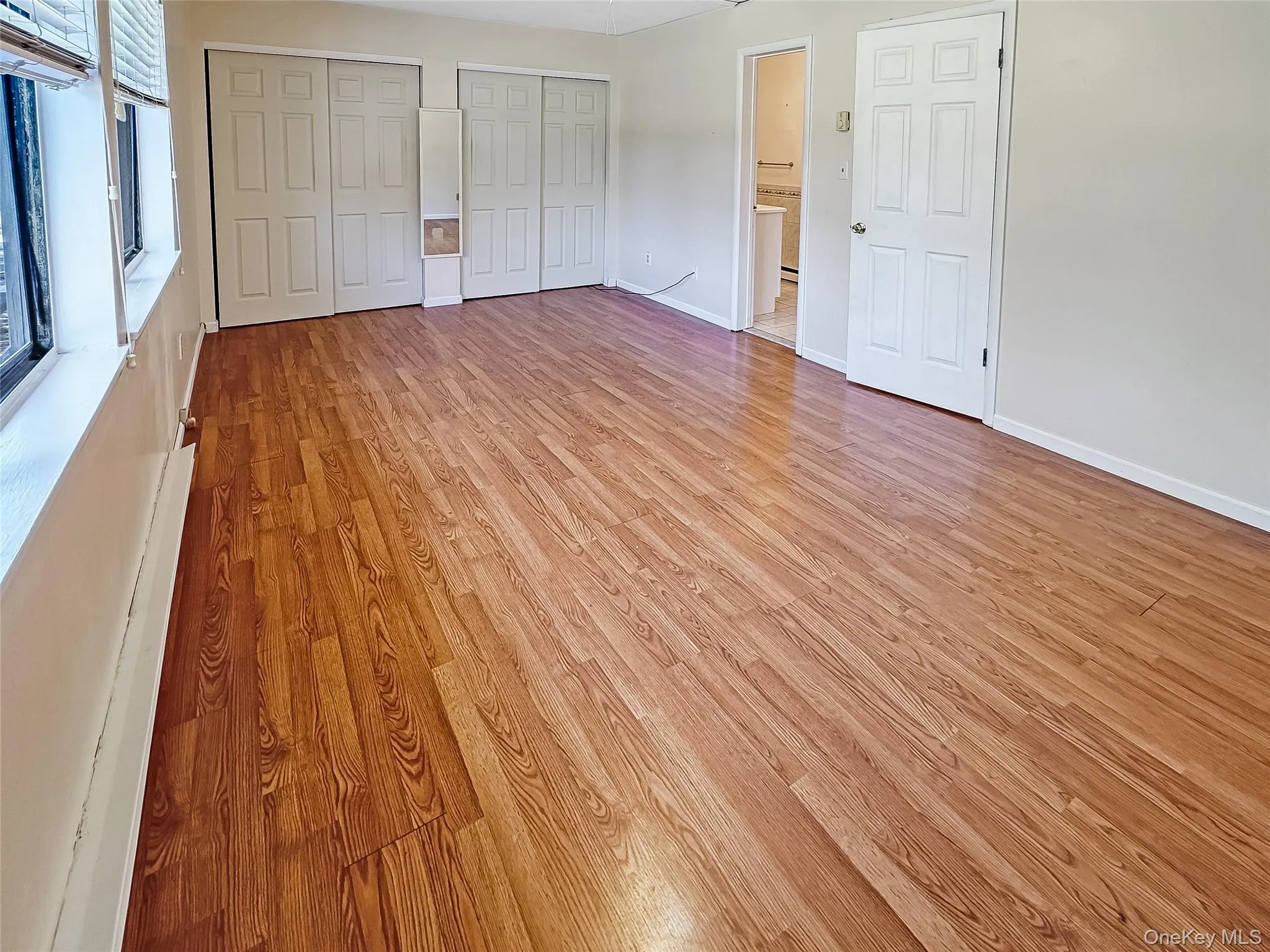 Unfurnished bedroom with multiple closets, light wood-style flooring, and baseboard heating Unfurnished bedroom with multiple closets, light wood-style flooring, and baseboard heating