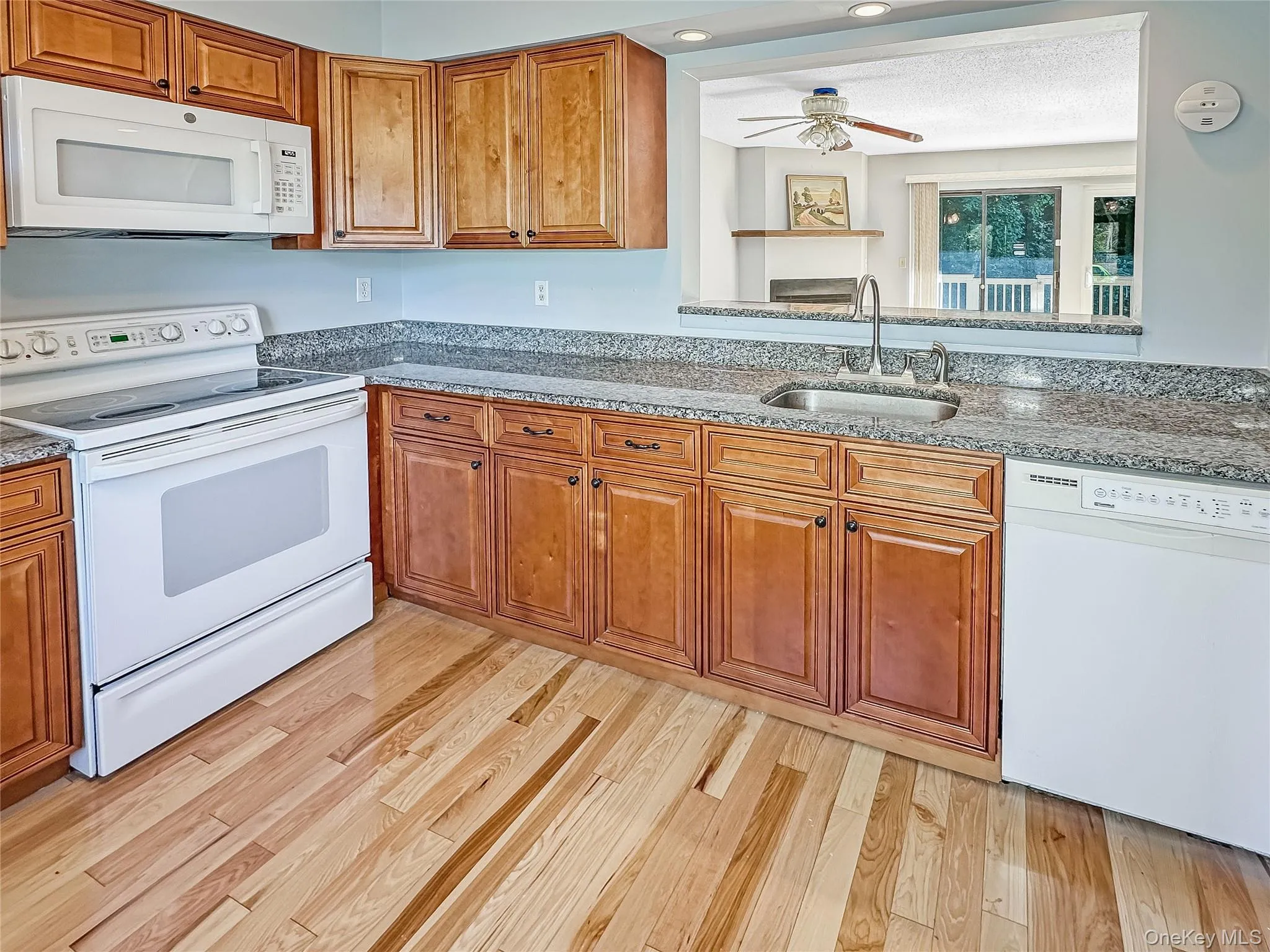Kitchen with white appliances, light stone counters, brown cabinetry, and recessed lighting Kitchen with white appliances, light stone counters, brown cabinetry, and recessed lighting