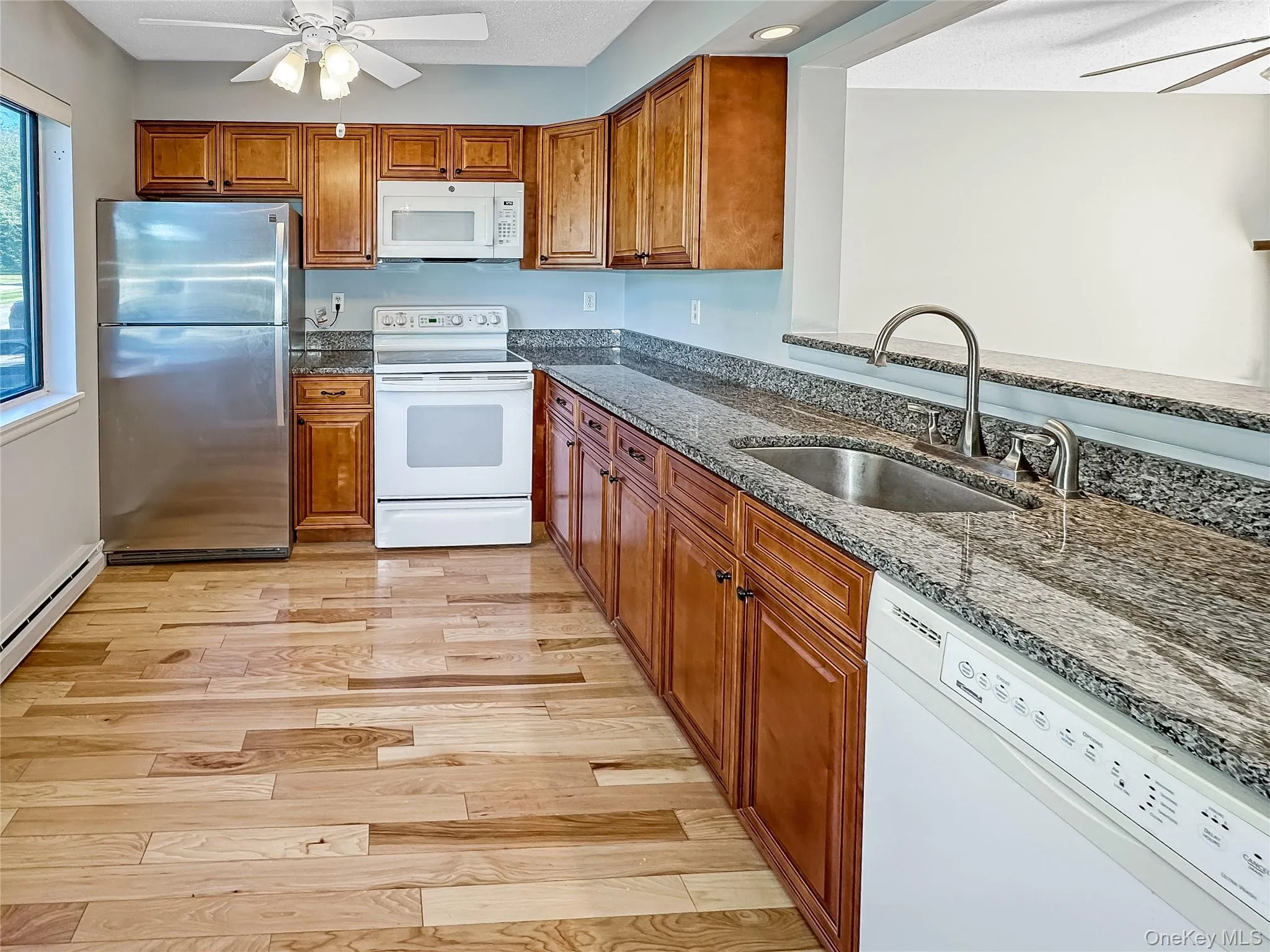 Kitchen with ceiling fan, white appliances, dark stone counters, and brown cabinetry Kitchen with ceiling fan, white appliances, dark stone counters, and brown cabinetry