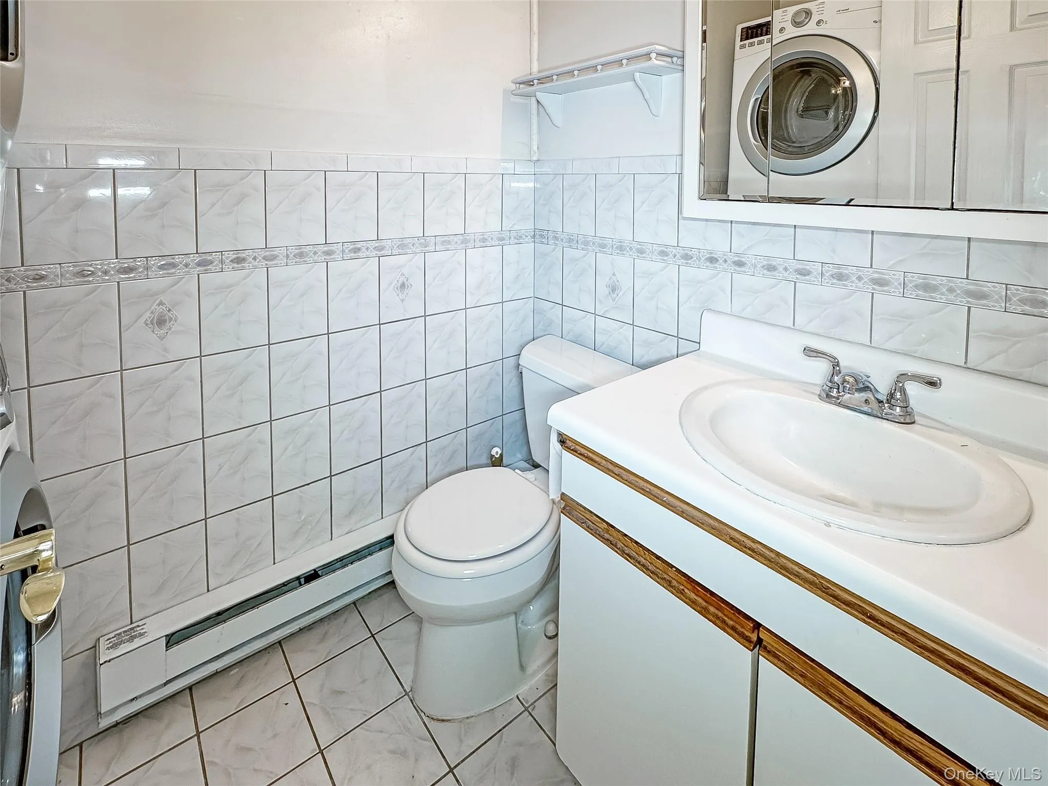 Half bath with washer / dryer, a baseboard heating unit, vanity, tile walls, and light tile patterned floors Half bath with washer / dryer, a baseboard heating unit, vanity, tile walls, and light tile patterned floors