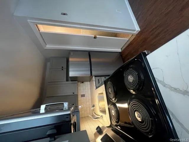 Kitchen with gray cabinets, light countertops, stainless steel appliances, dark wood-style floors, and backsplash Kitchen with gray cabinets, light countertops, stainless steel appliances, dark wood-style floors, and backsplash