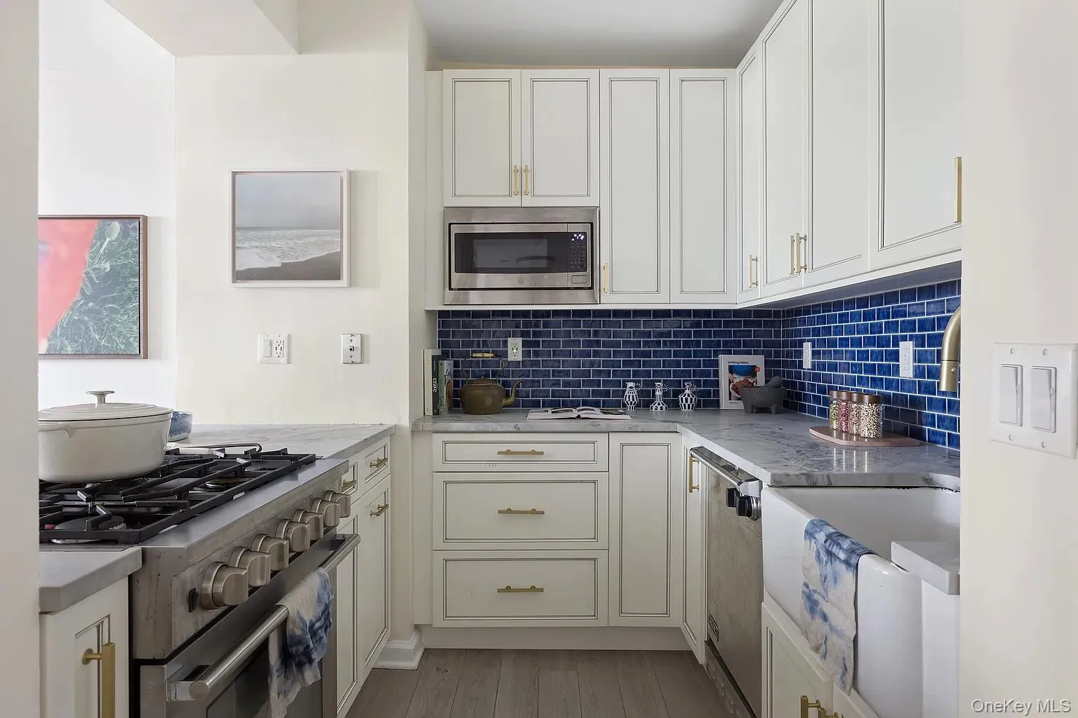 Kitchen with appliances with stainless steel finishes, tasteful backsplash, light stone countertops, light wood finished floors, and white cabinetry Kitchen with appliances with stainless steel finishes, tasteful backsplash, light stone countertops, light wood finished floors, and white cabinetry