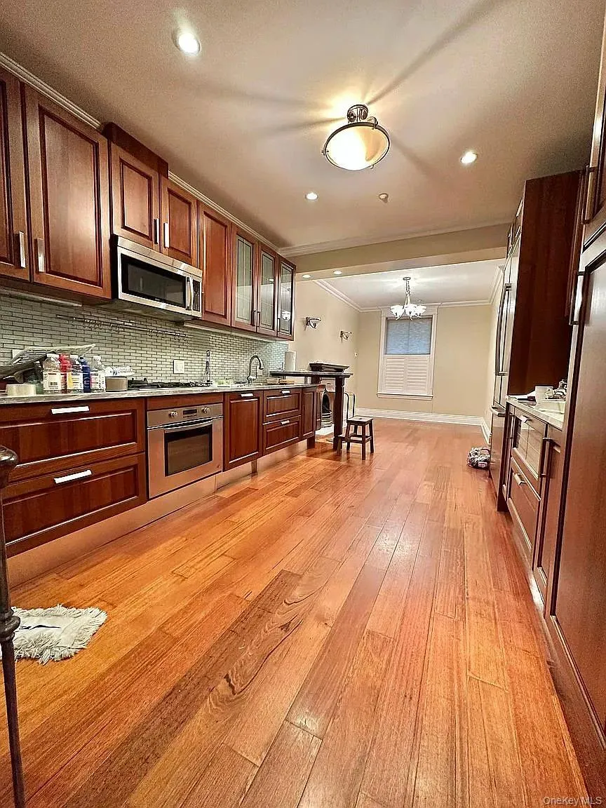 Kitchen with stainless steel appliances, light wood-type flooring, ornamental molding, backsplash, and glass insert cabinets Kitchen with stainless steel appliances, light wood-type flooring, ornamental molding, backsplash, and glass insert cabinets