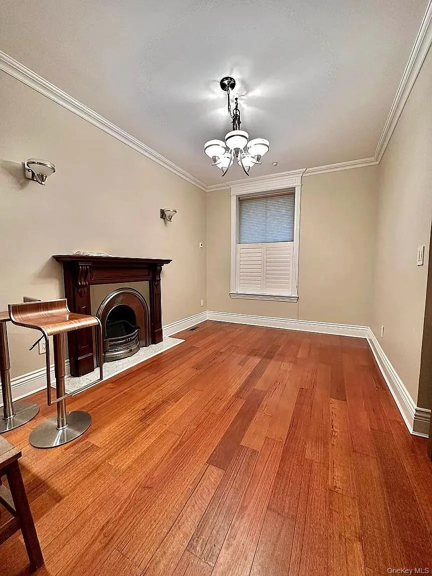 Unfurnished living room with a fireplace, light wood-type flooring, crown molding, and a chandelier Unfurnished living room with a fireplace, light wood-type flooring, crown molding, and a chandelier