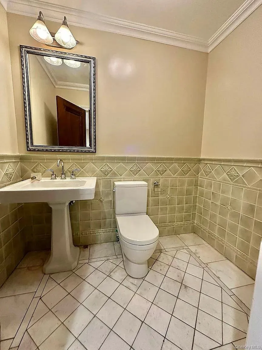 Half bathroom with ornamental molding, tile walls, light tile patterned flooring, and wainscoting Half bathroom with ornamental molding, tile walls, light tile patterned flooring, and wainscoting