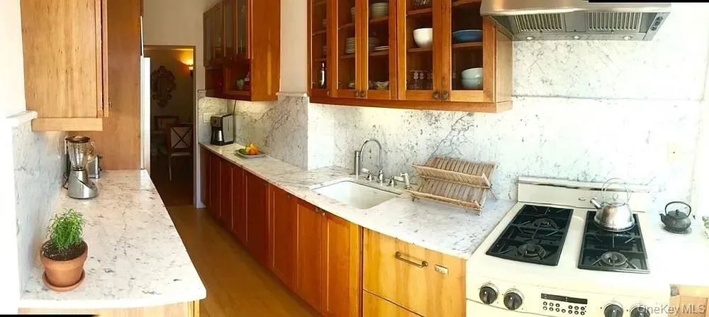 Kitchen with white gas stove, wall chimney exhaust hood, tasteful backsplash, glass insert cabinets, and light stone countertops Kitchen with white gas stove, wall chimney exhaust hood, tasteful backsplash, glass insert cabinets, and light stone countertops