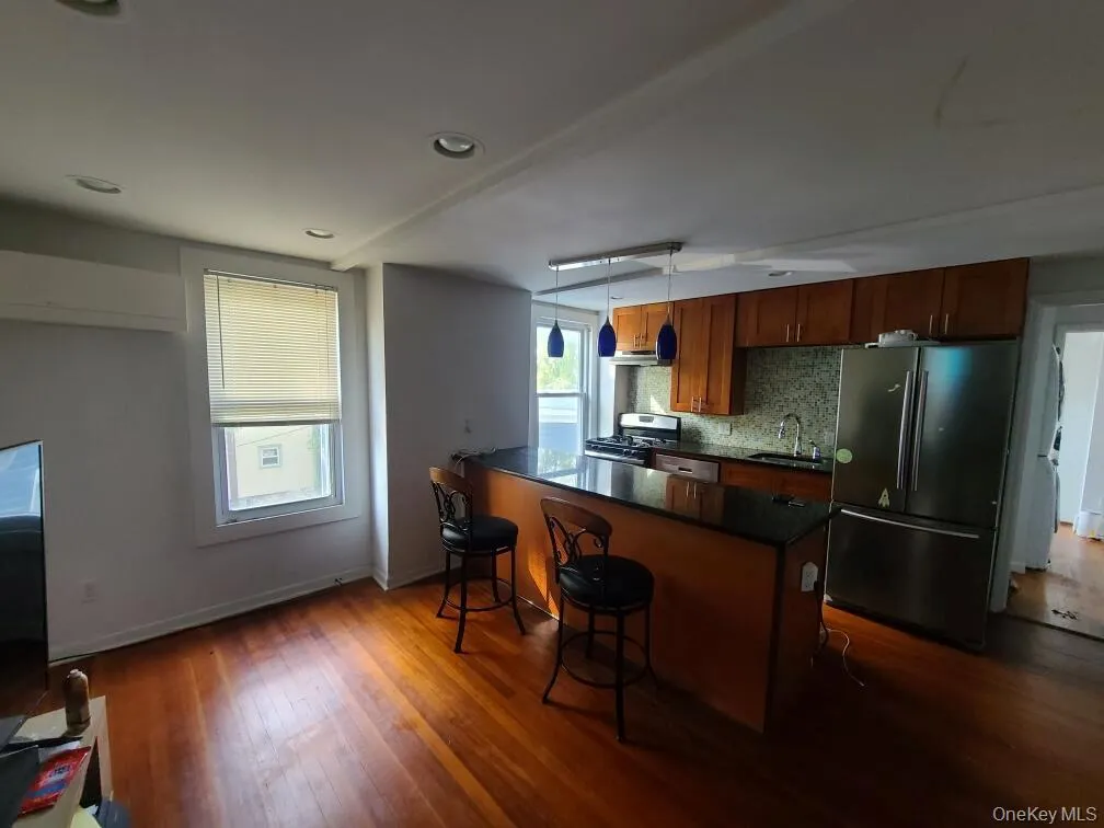 Kitchen featuring appliances with stainless steel finishes, a breakfast bar, brown cabinets, backsplash, and dark stone counters Kitchen featuring appliances with stainless steel finishes, a breakfast bar, brown cabinets, backsplash, and dark stone counters