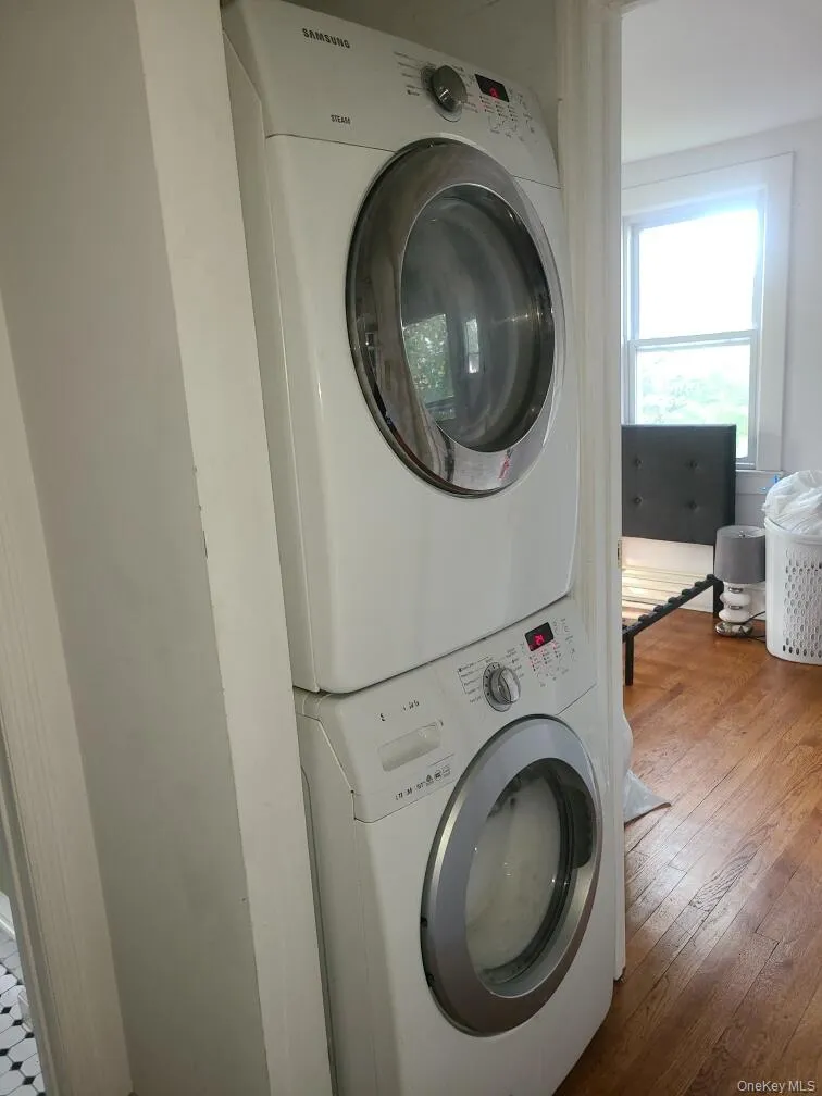 Laundry room featuring stacked washing machine and dryer and wood-type flooring Laundry room featuring stacked washing machine and dryer and wood-type flooring
