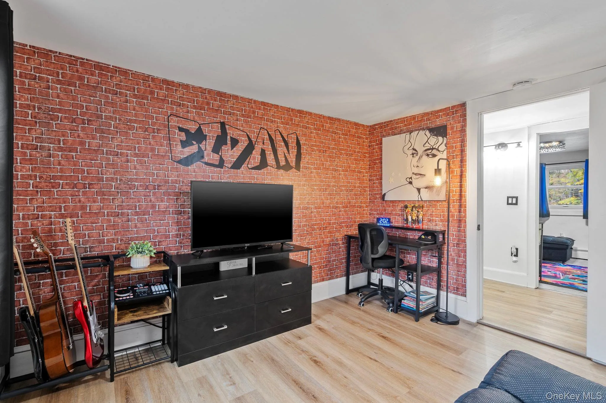 Living room featuring light wood finished floors, an office area, and brick wall Living room featuring light wood finished floors, an office area, and brick wall