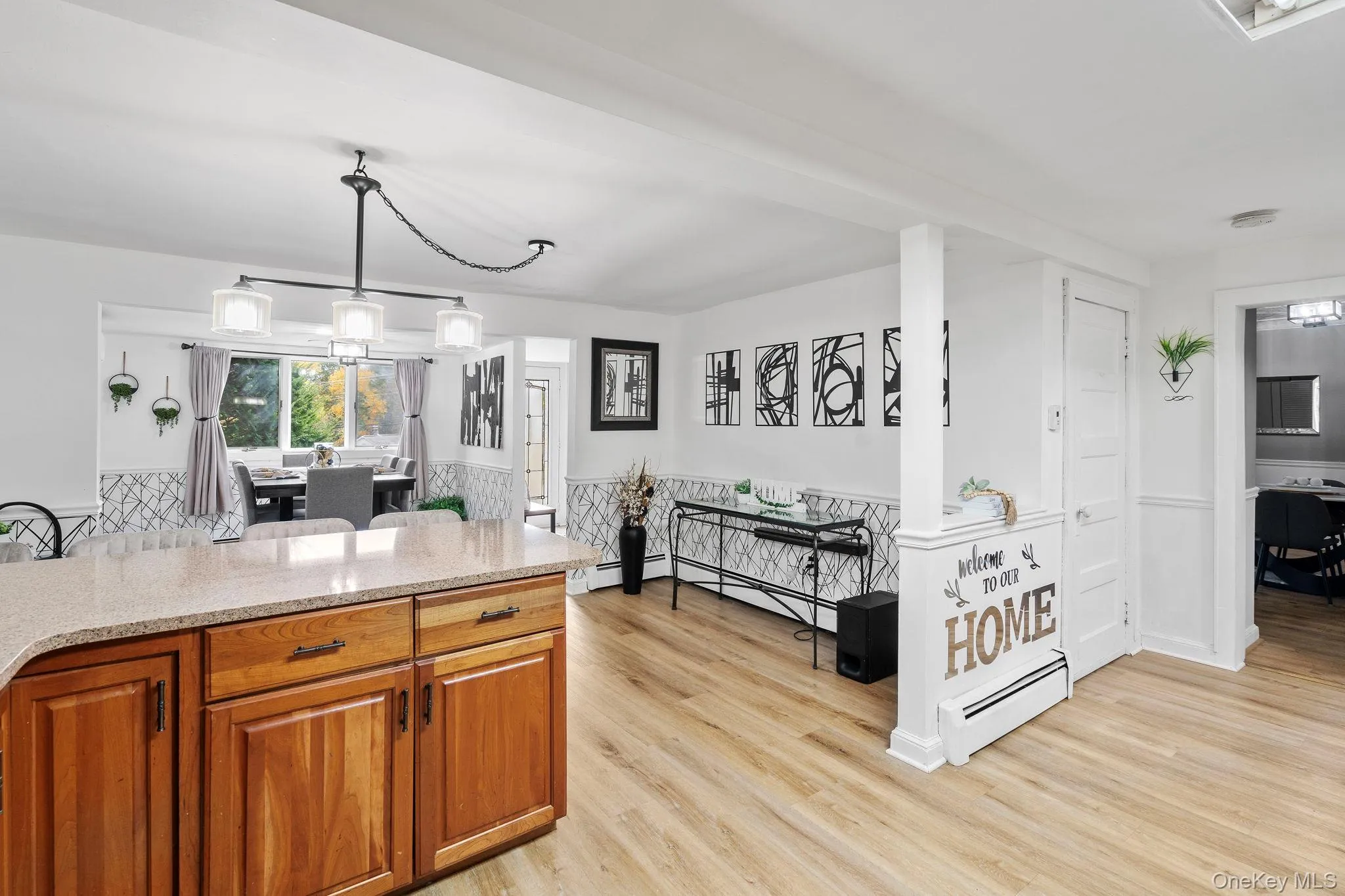 Kitchen with brown cabinets, light stone counters, light wood-style floors, pendant lighting, and baseboard heating Kitchen with brown cabinets, light stone counters, light wood-style floors, pendant lighting, and baseboard heating