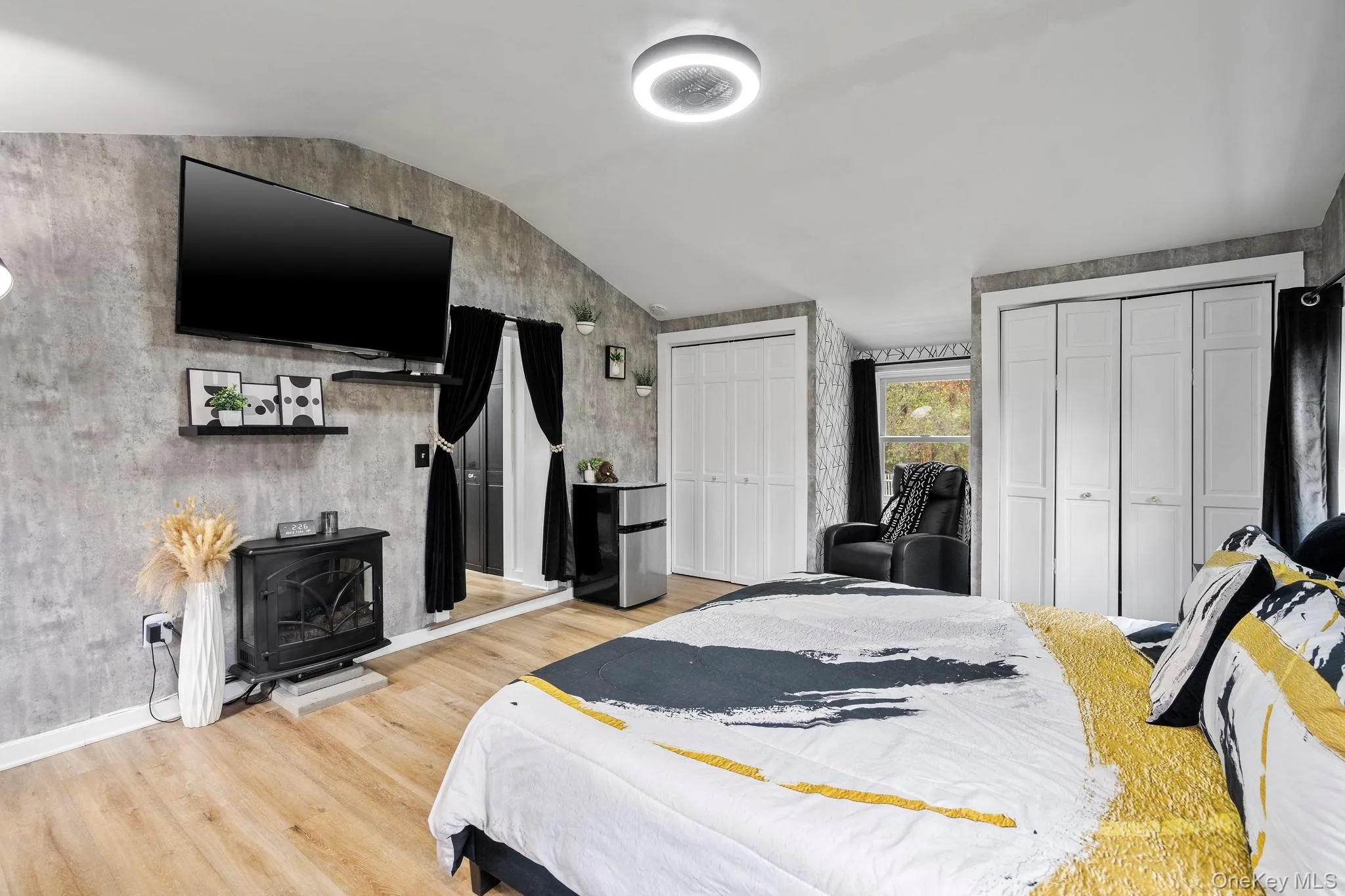 Bedroom with lofted ceiling, two closets, a wood stove, light wood finished floors, and freestanding refrigerator Bedroom with lofted ceiling, two closets, a wood stove, light wood finished floors, and freestanding refrigerator