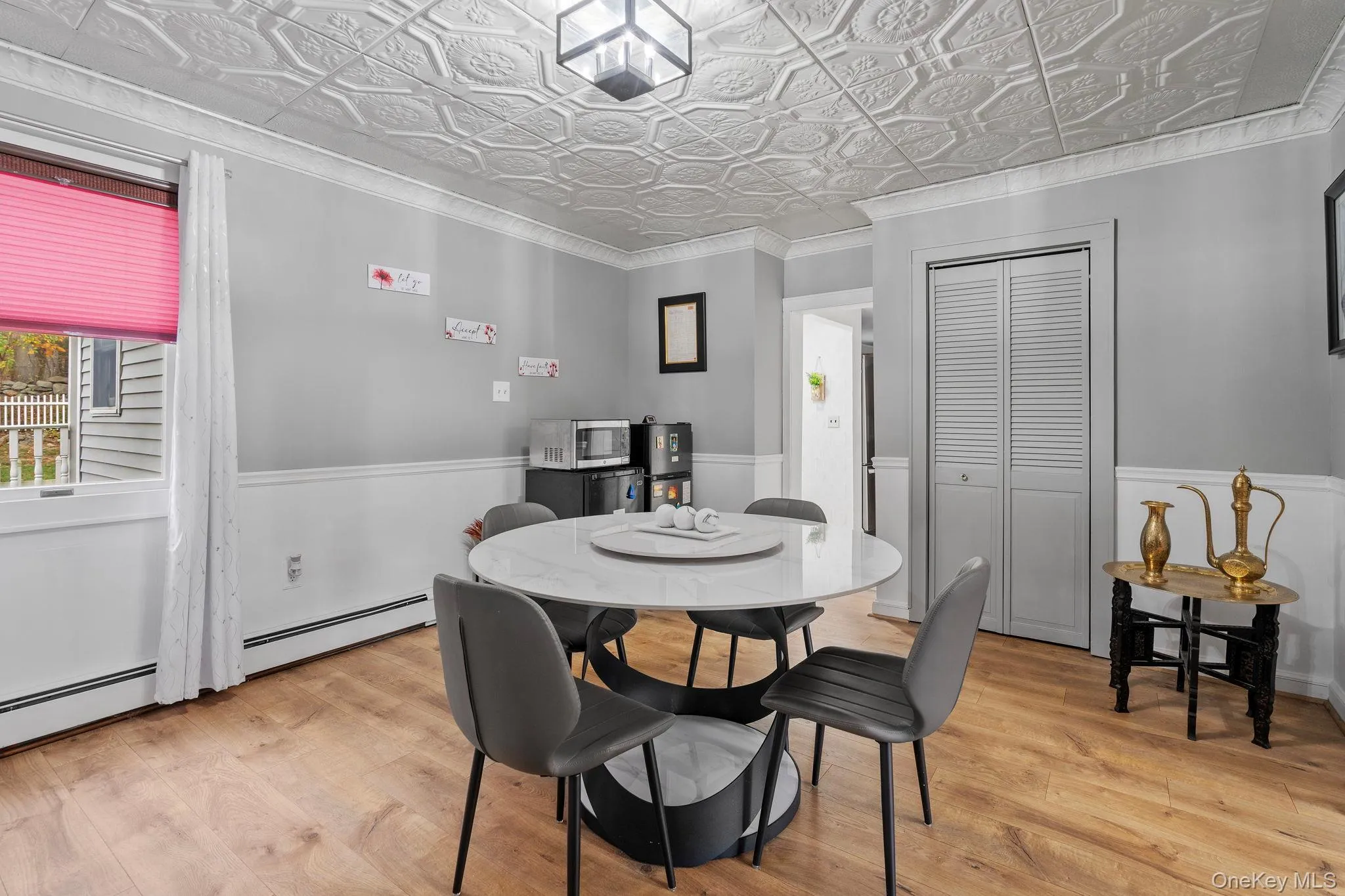Dining area with ornamental molding, light wood-type flooring, an ornate ceiling, baseboard heating, and wainscoting Dining area with ornamental molding, light wood-type flooring, an ornate ceiling, baseboard heating, and wainscoting