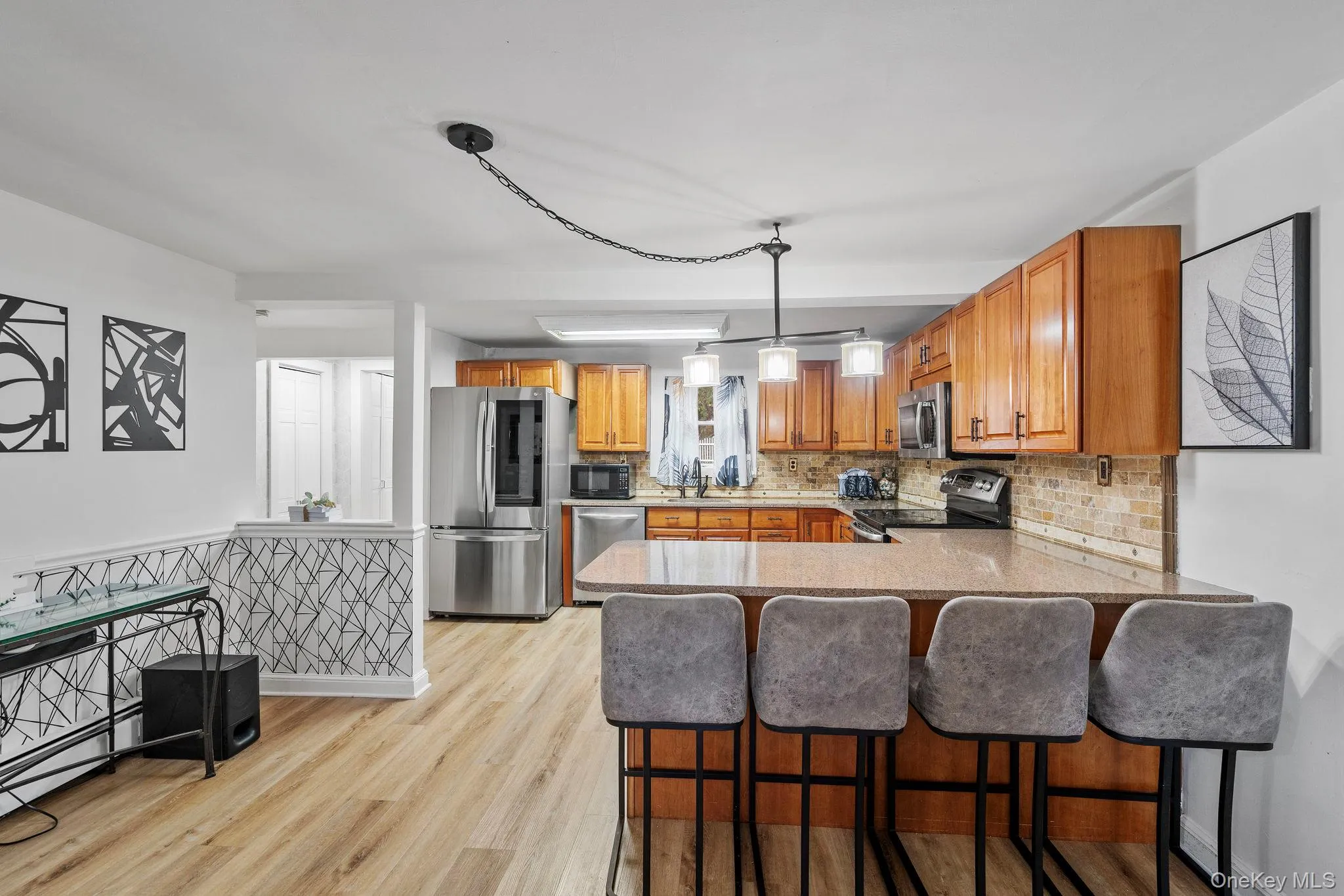 Kitchen featuring brown cabinets, backsplash, a kitchen bar, light wood-style flooring, and appliances with stainless steel finishes Kitchen featuring brown cabinets, backsplash, a kitchen bar, light wood-style flooring, and appliances with stainless steel finishes