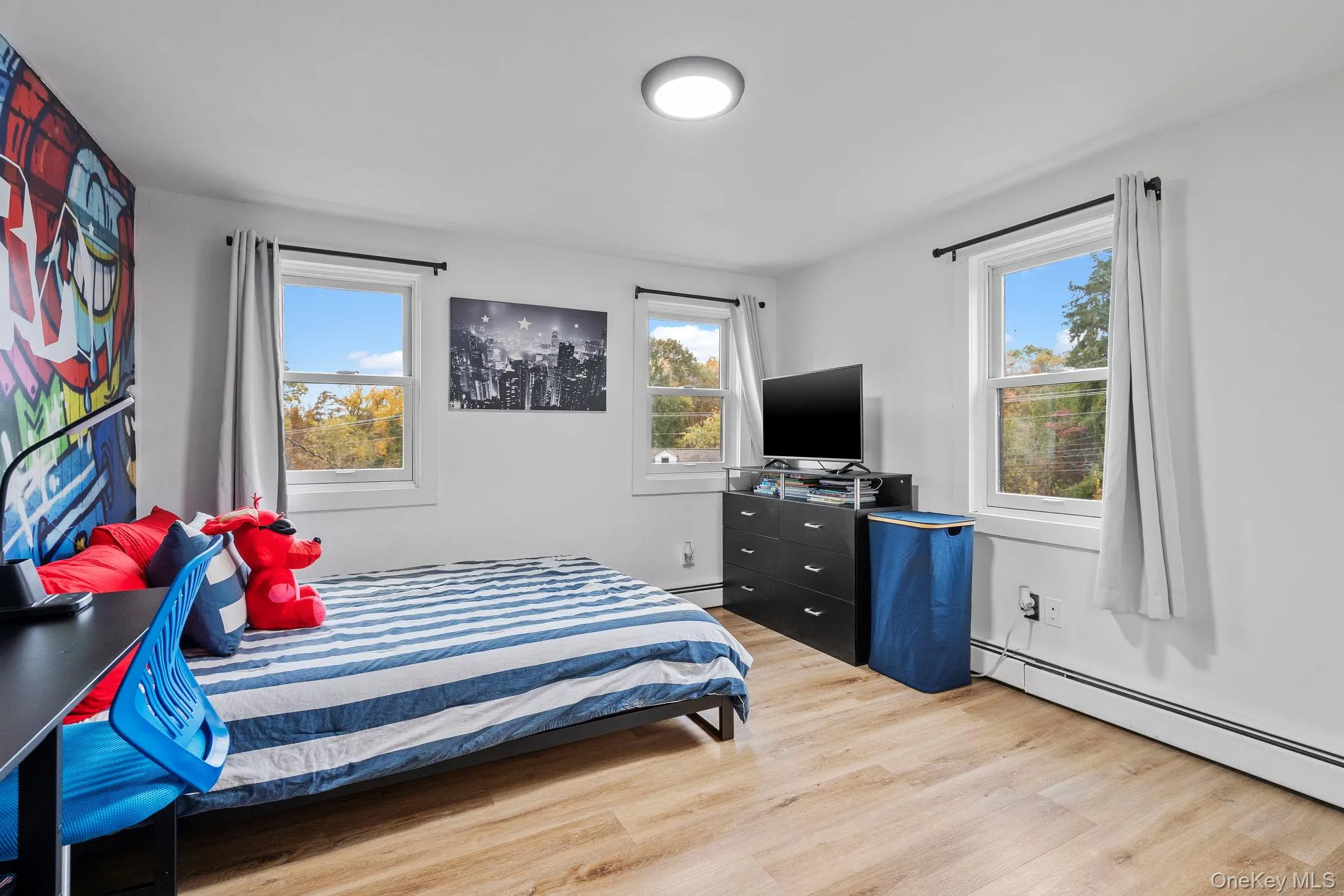 Bedroom with multiple windows, light wood-style flooring, and baseboard heating Bedroom with multiple windows, light wood-style flooring, and baseboard heating