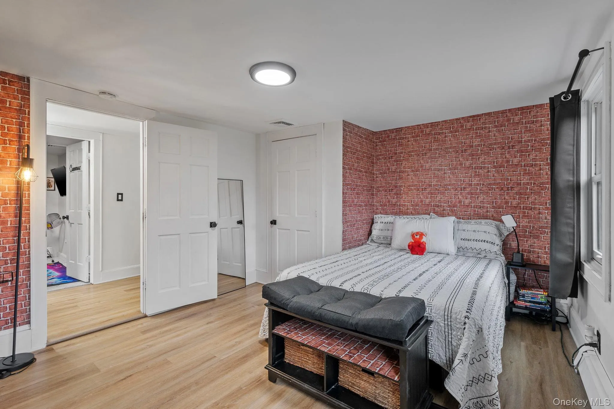 Bedroom featuring brick wall, light wood-type flooring, and a closet Bedroom featuring brick wall, light wood-type flooring, and a closet