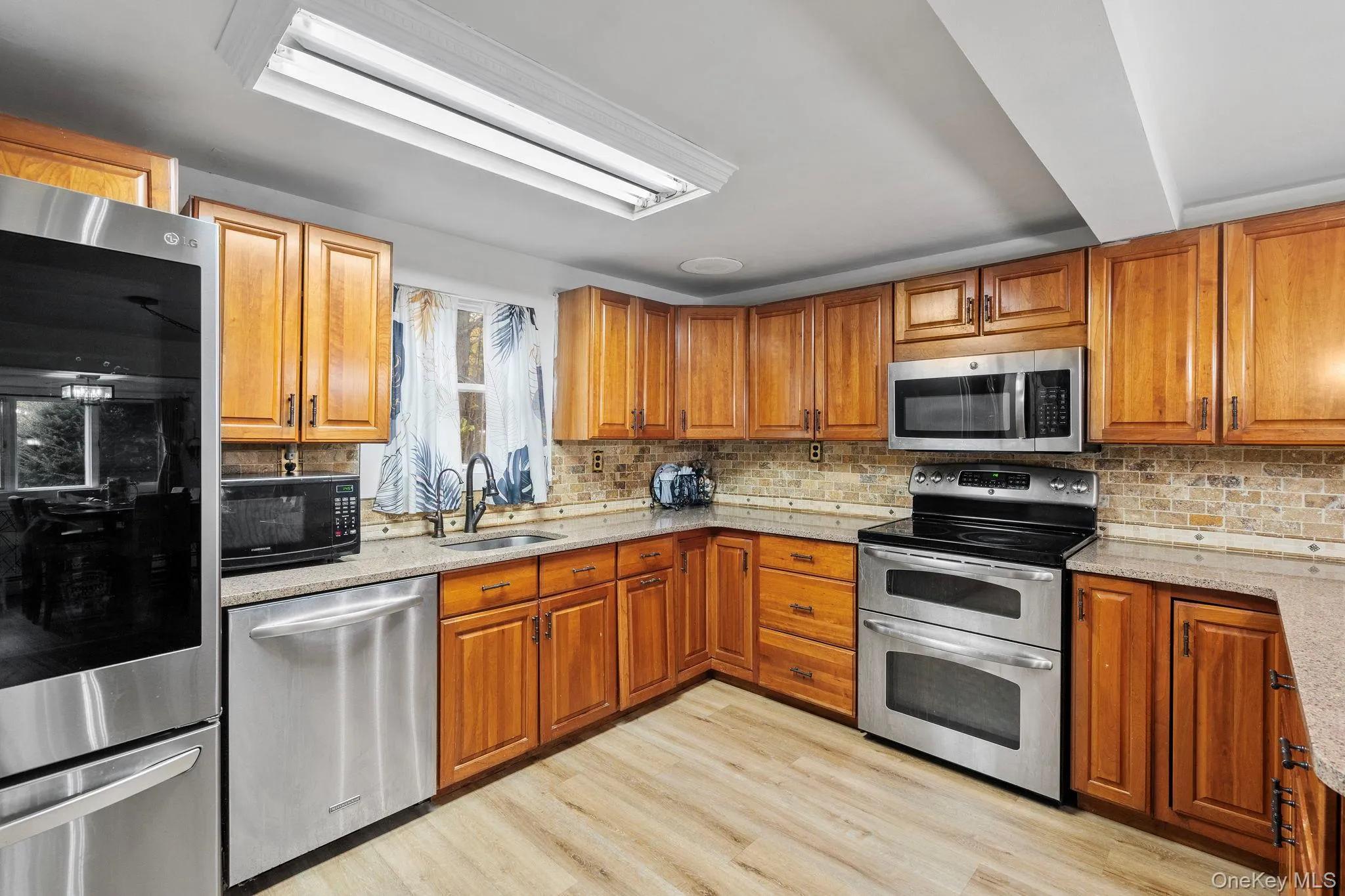 Kitchen featuring stainless steel appliances, brown cabinets, and light stone countertops Kitchen featuring stainless steel appliances, brown cabinets, and light stone countertops