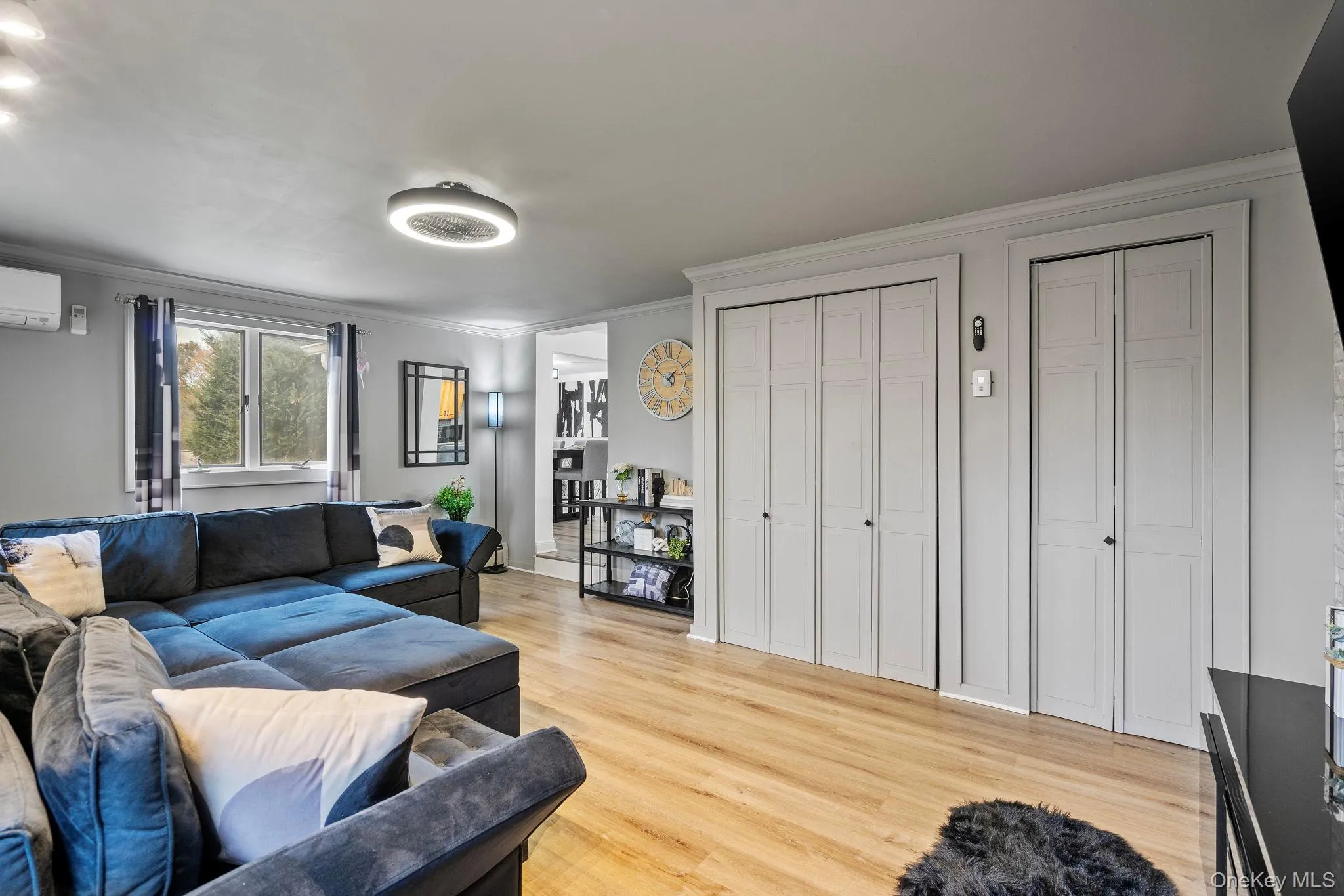 Living area with light wood-style flooring, ornamental molding, and an AC wall unit Living area with light wood-style flooring, ornamental molding, and an AC wall unit