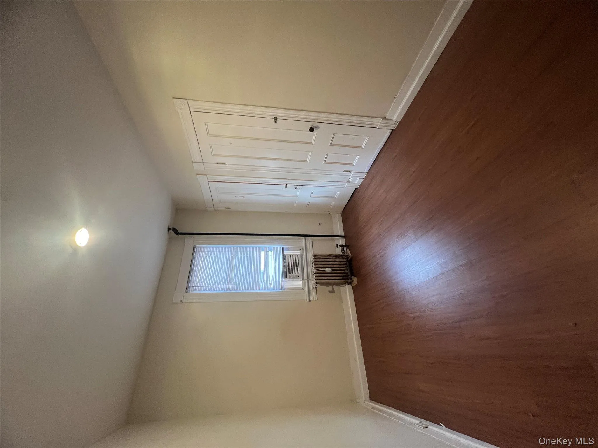 Unfurnished bedroom featuring dark wood-type flooring, two closets, radiator heating unit, and cooling unit Unfurnished bedroom featuring dark wood-type flooring, two closets, radiator heating unit, and cooling unit