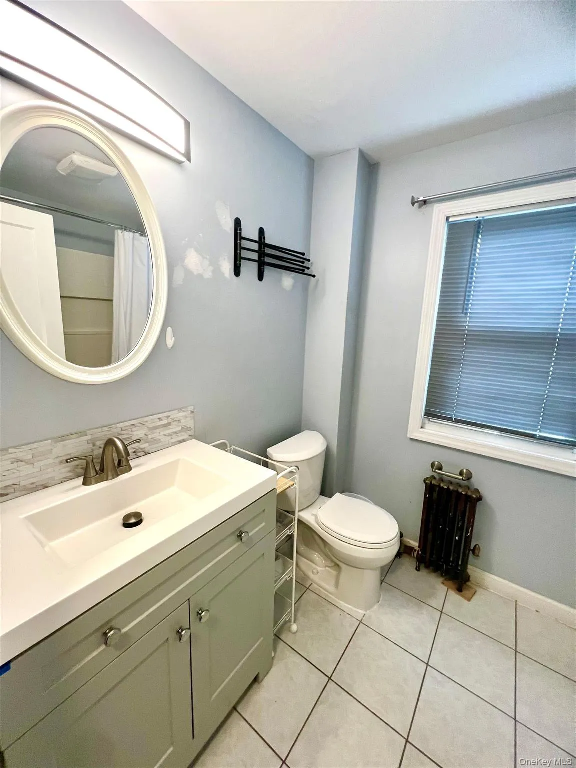 Bathroom featuring vanity, radiator, light tile patterned flooring, and curtained shower Bathroom featuring vanity, radiator, light tile patterned flooring, and curtained shower