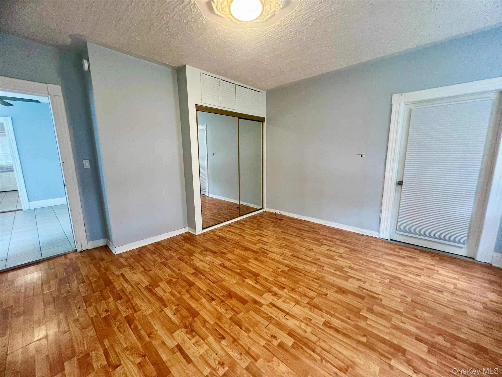 Unfurnished bedroom featuring a textured ceiling, light wood-type flooring, and a closet Unfurnished bedroom featuring a textured ceiling, light wood-type flooring, and a closet