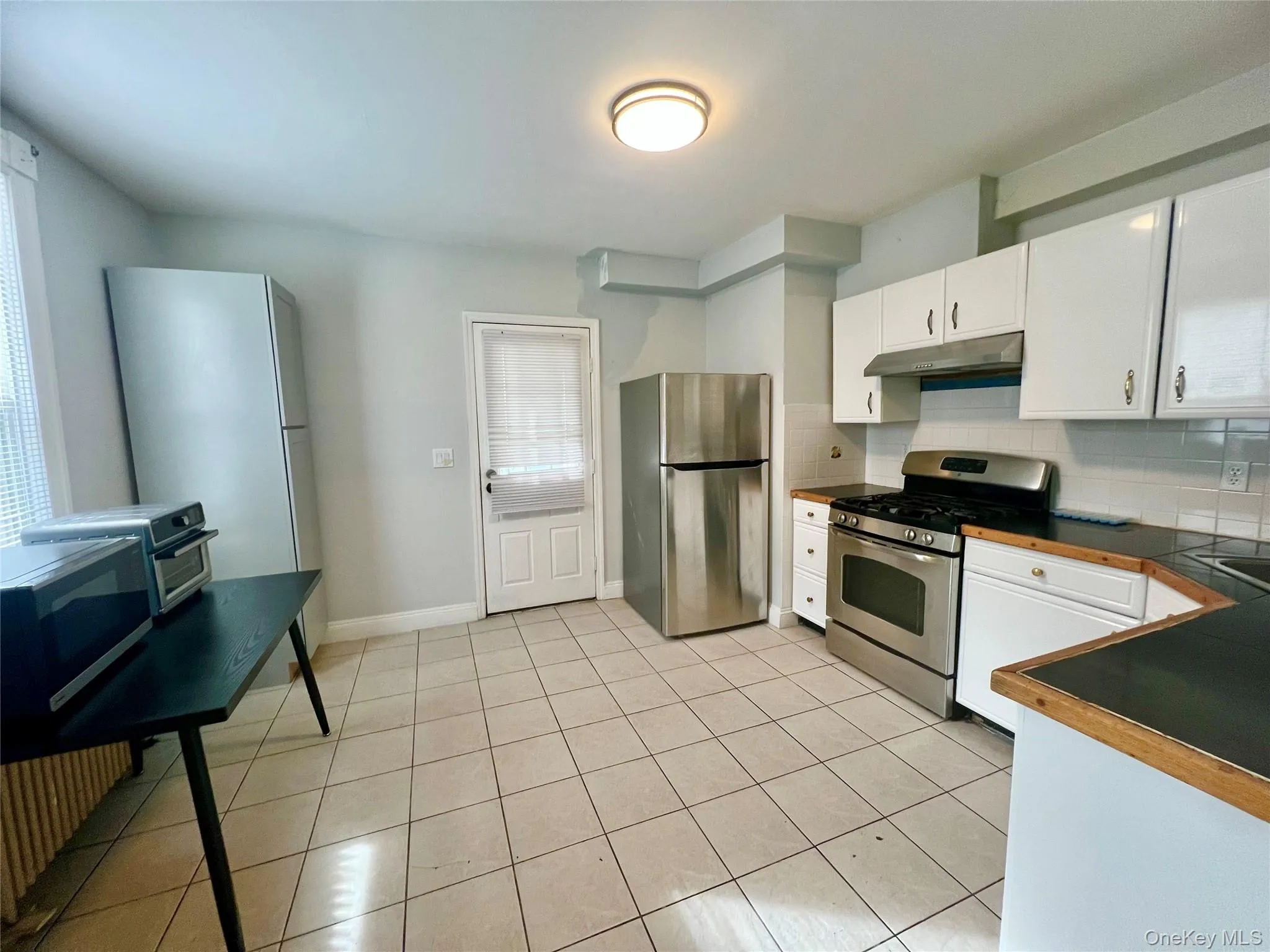 Kitchen featuring stainless steel appliances, tasteful backsplash, white cabinetry, dark countertops, and light tile patterned floors Kitchen featuring stainless steel appliances, tasteful backsplash, white cabinetry, dark countertops, and light tile patterned floors